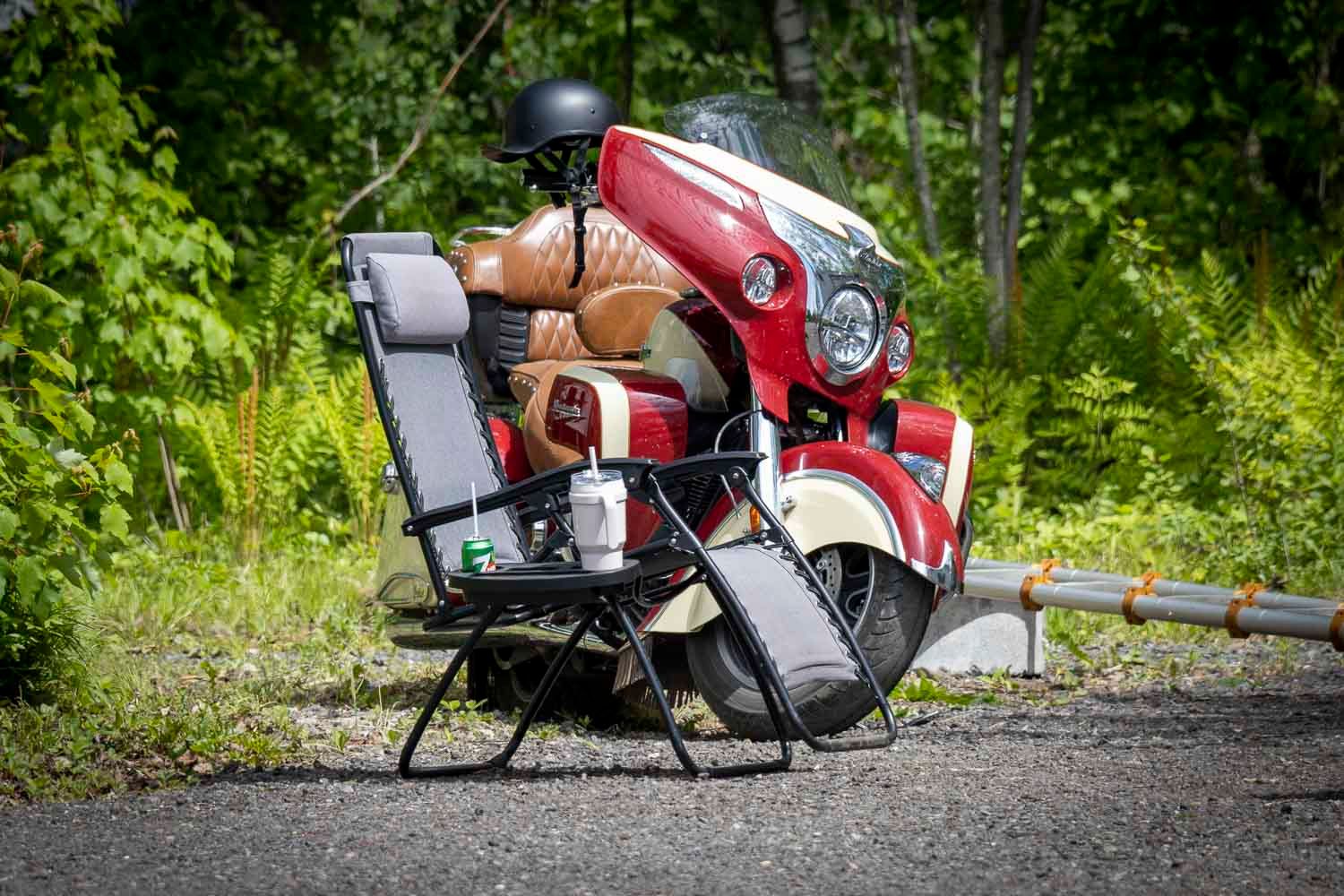 Red Indian motorcycle parked beside a folding chair on a rural road surrounded by greenery.