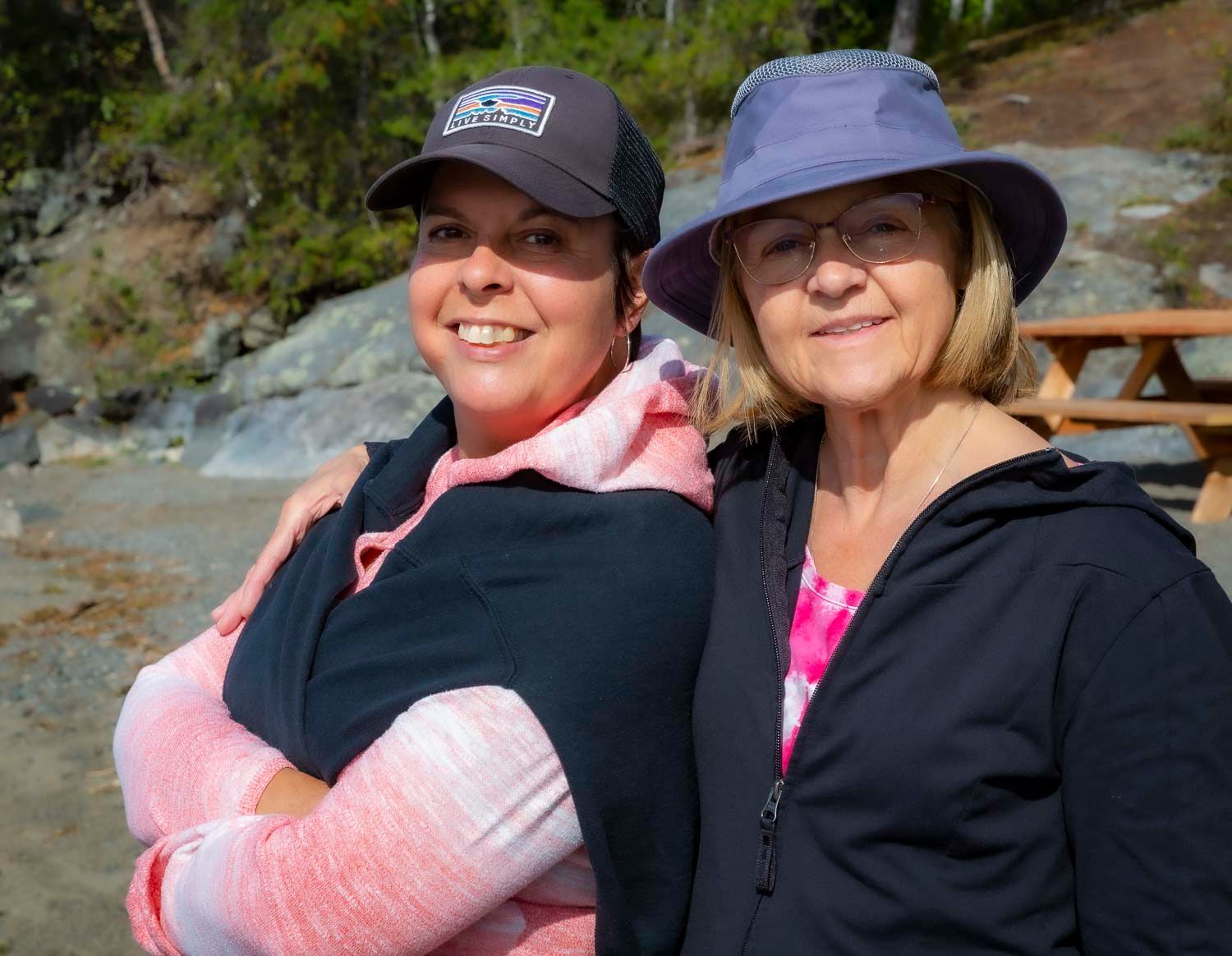 Two smiling women wearing hats posing together outdoors near rocky mountain terrain.