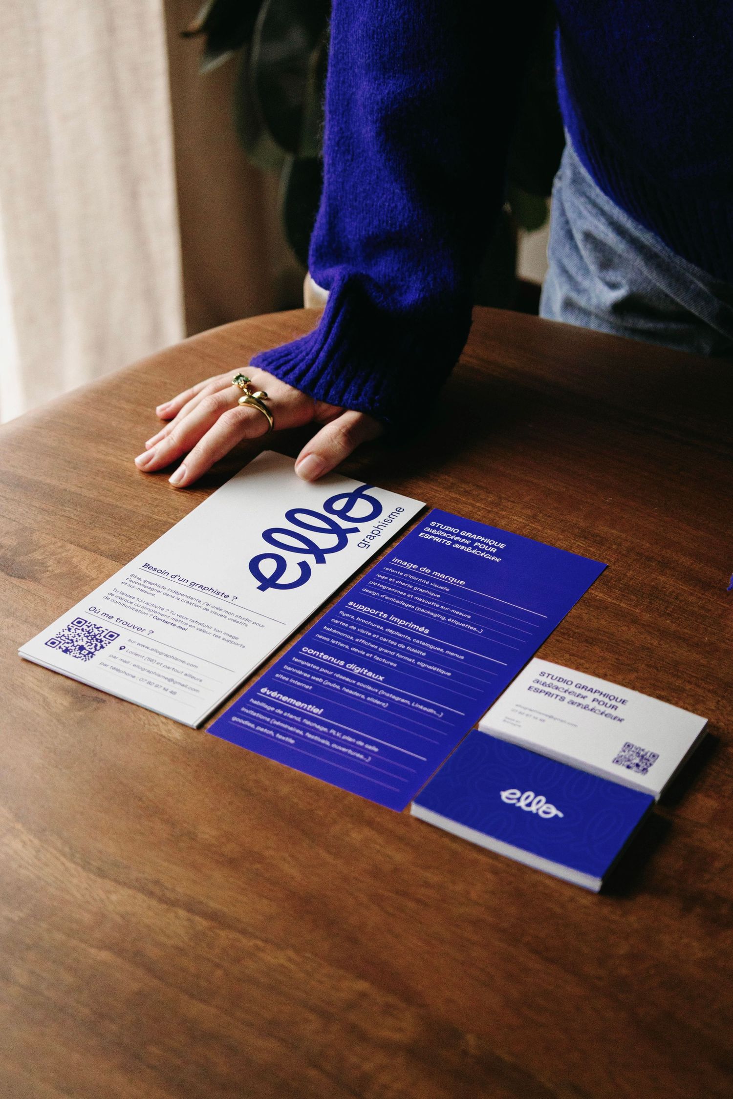 Person in blue sweater presenting blue branded brochures and business cards on wooden table.