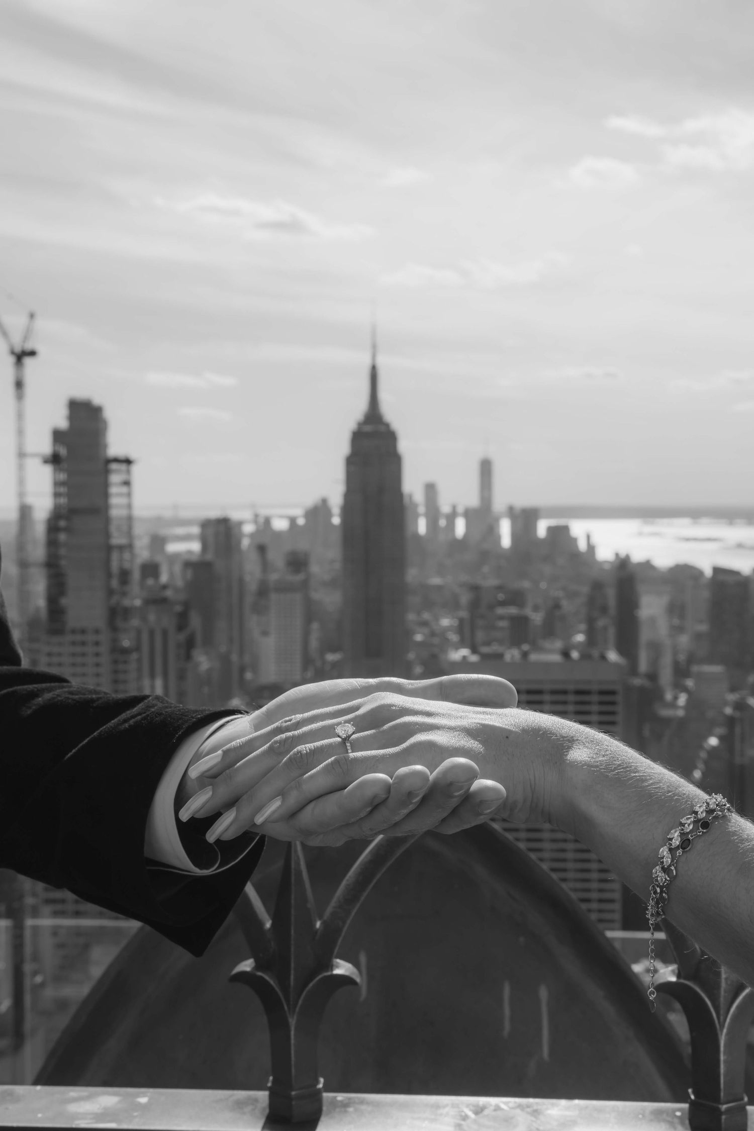 Black and white closeup of hands touching against New York City skyline backdrop.