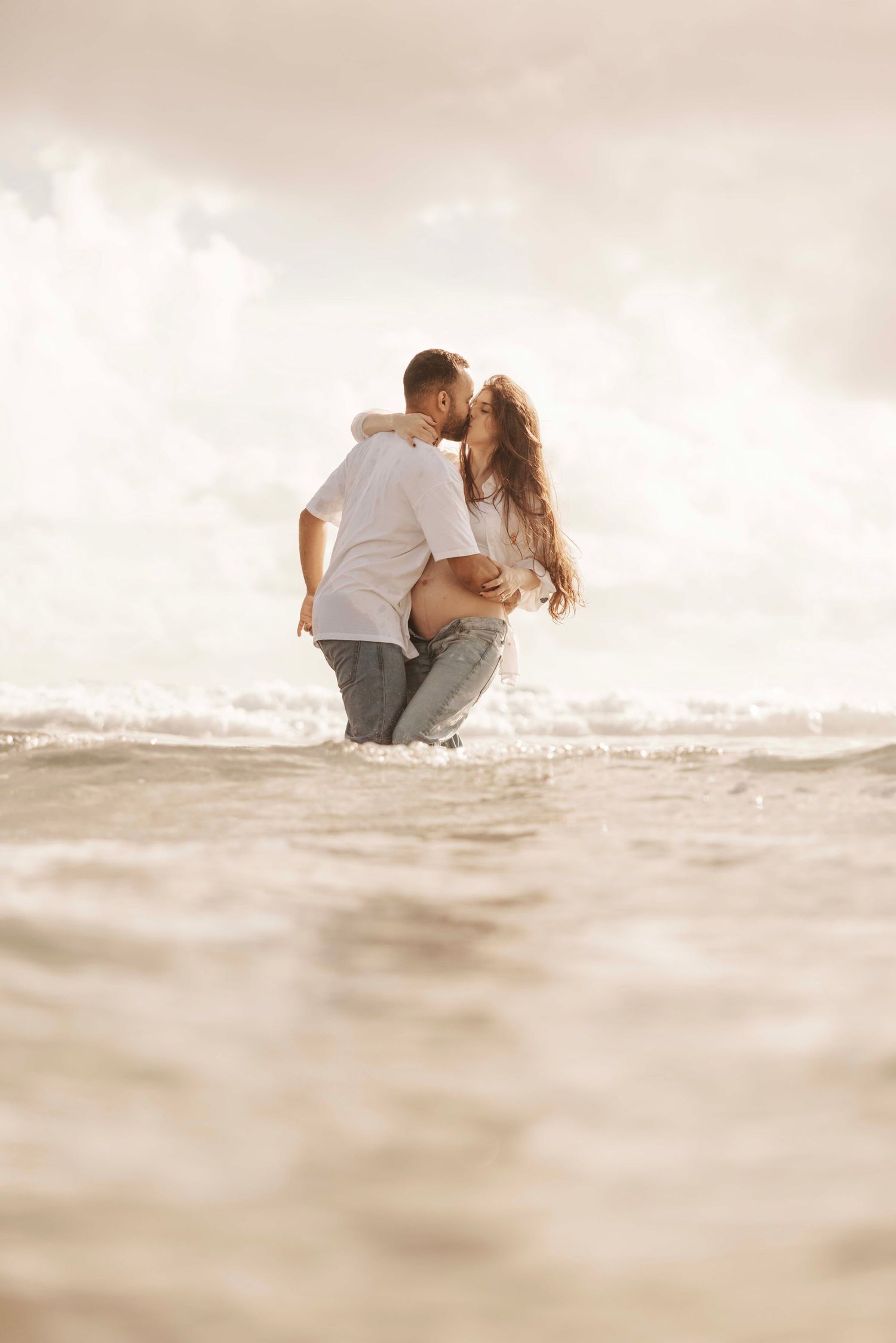 Romantic couple embracing in gentle ocean waves at sunset.