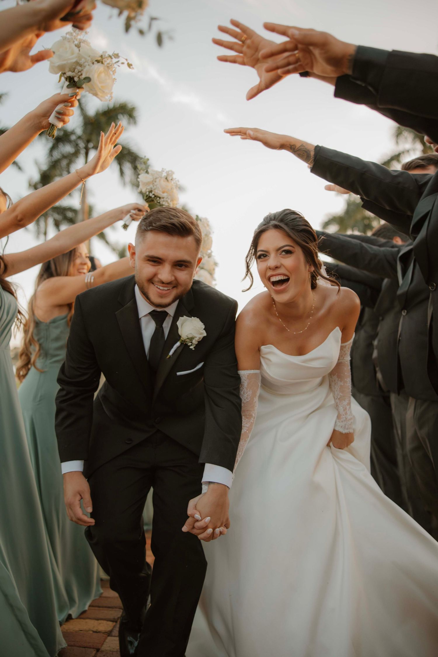 Wedding party celebrating with raised hands as couple walks under guest tunnel.