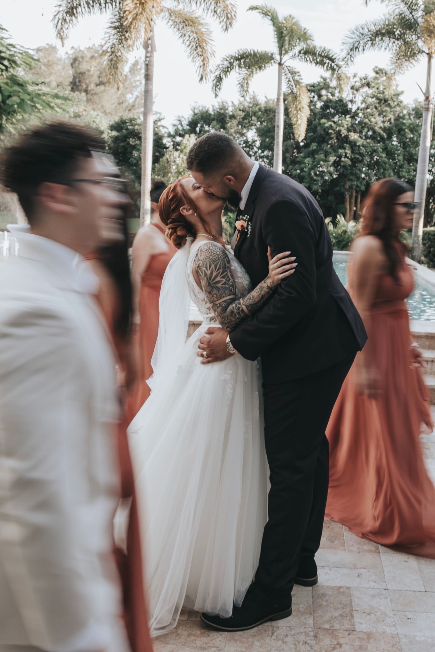 Newlyweds share a kiss during their wedding reception while guests move around them.