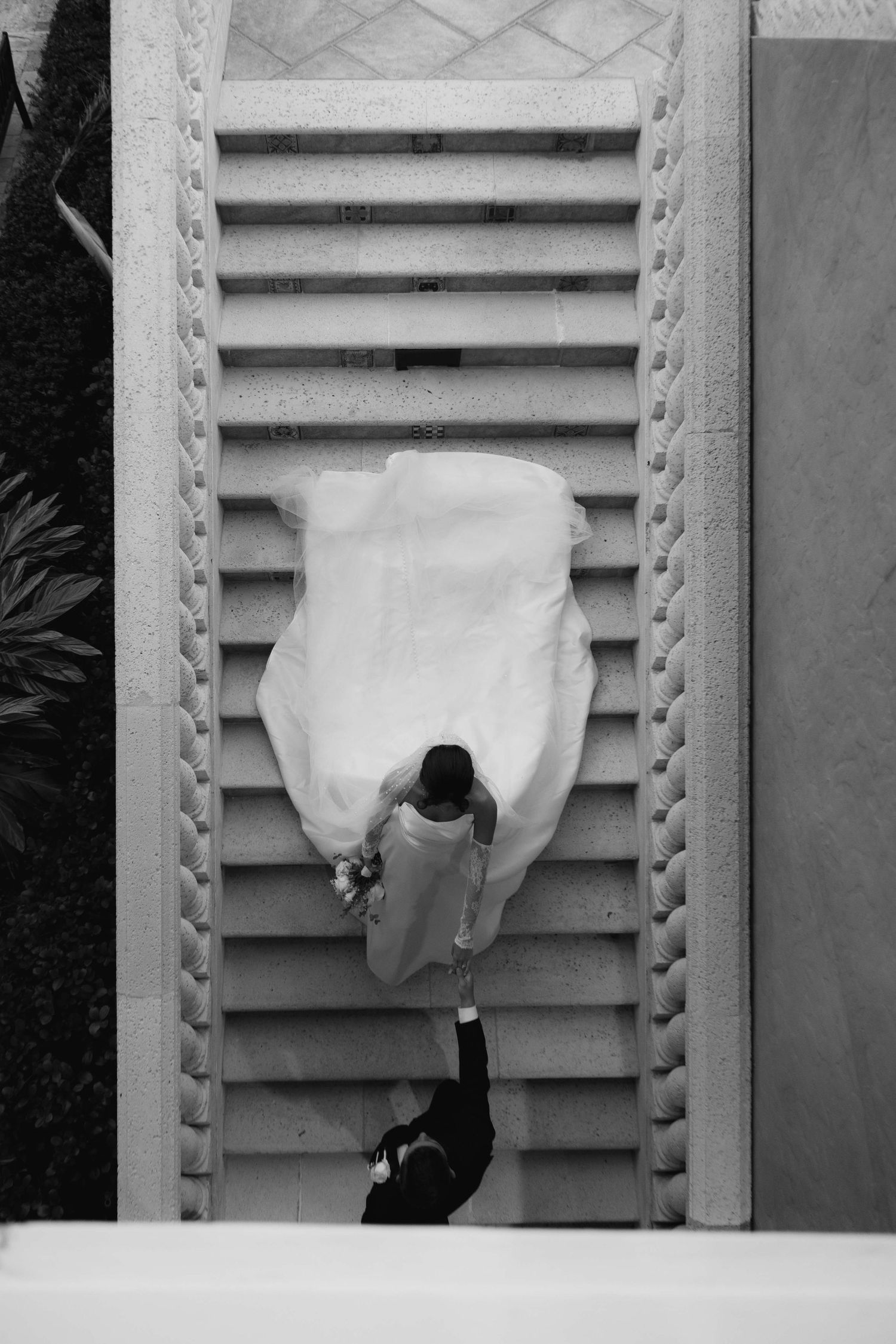 Black and white overhead shot of couple ascending ornate staircase.