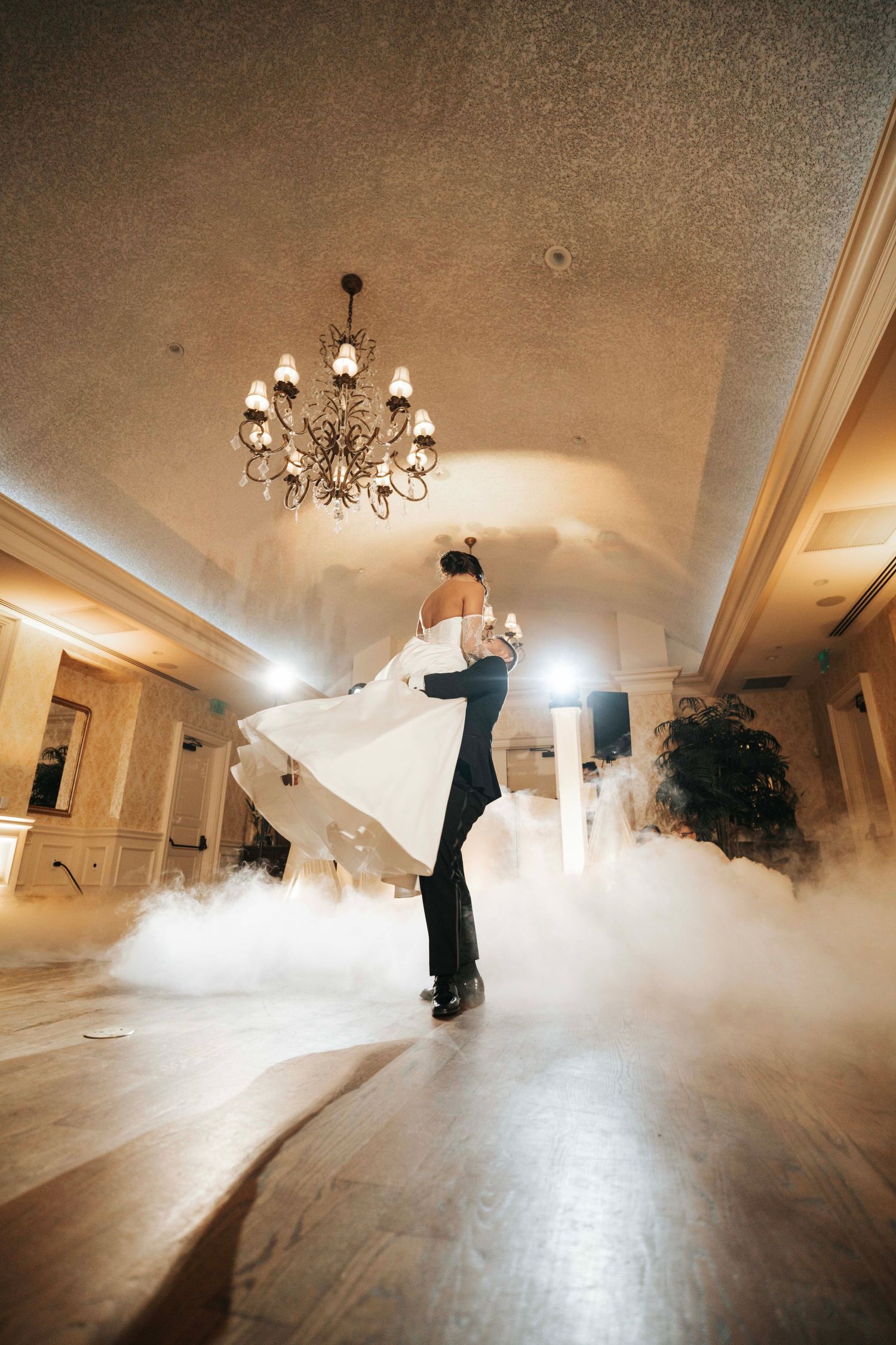 Romantic first dance in a ballroom with fog machine effects and elegant chandelier overhead.