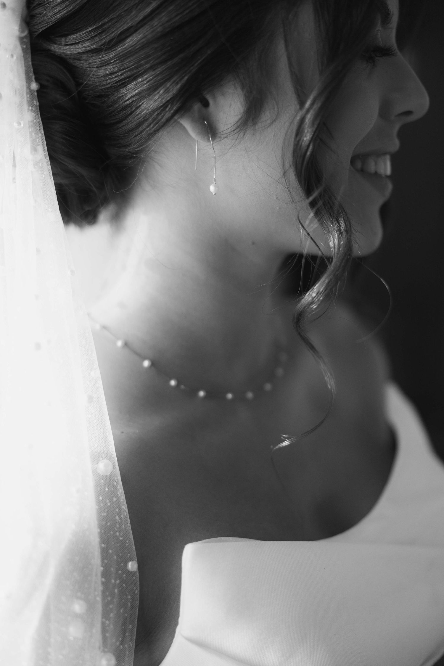 Black and white profile shot showing delicate bridal jewelry and veil details.