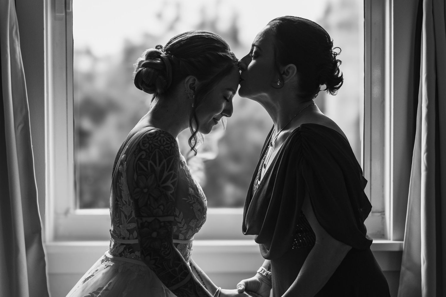 Intimate black and white photo of two people sharing a tender moment by a window.