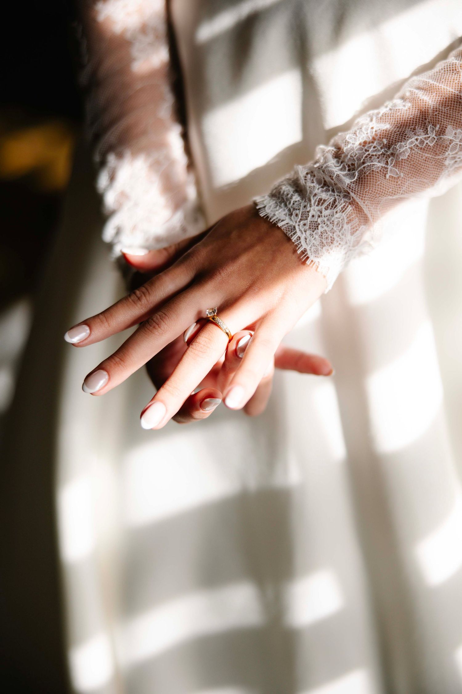 Close-up of bride's hand with engagement ring and lace sleeve details in natural light.