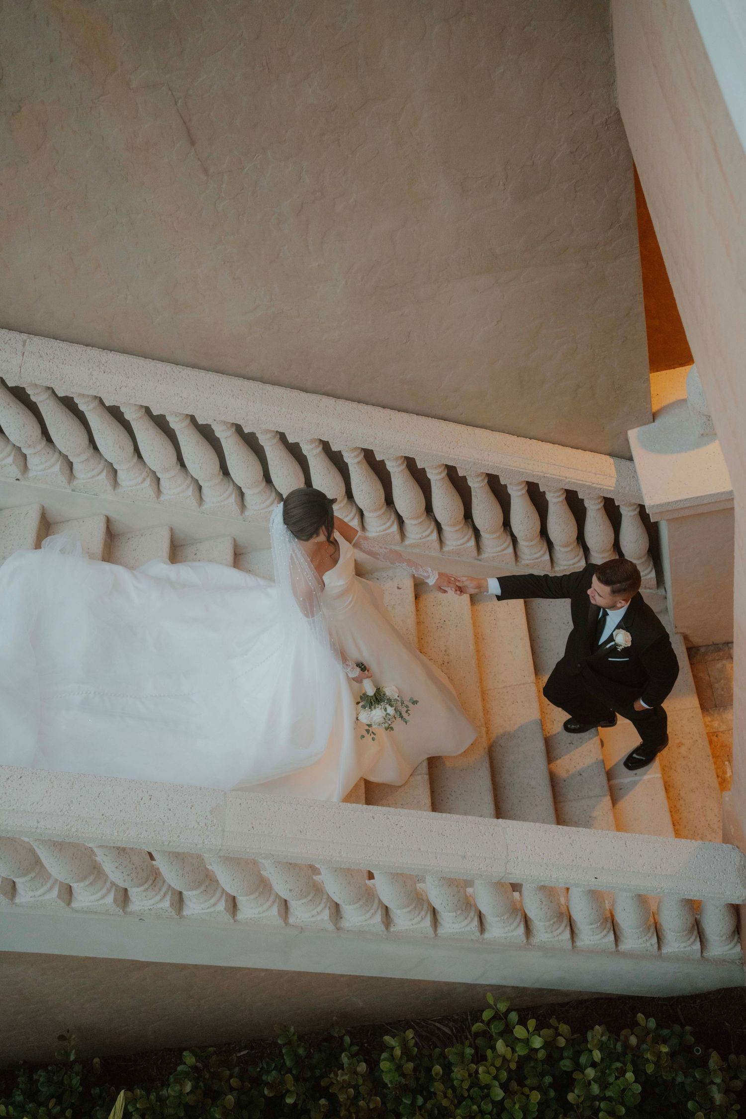 Couple ascending decorative white stone staircase at wedding venue.