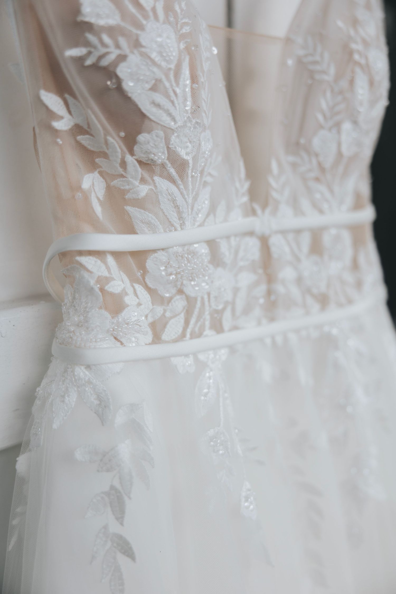 Close up detail of delicate floral lace pattern on white wedding dress bodice.