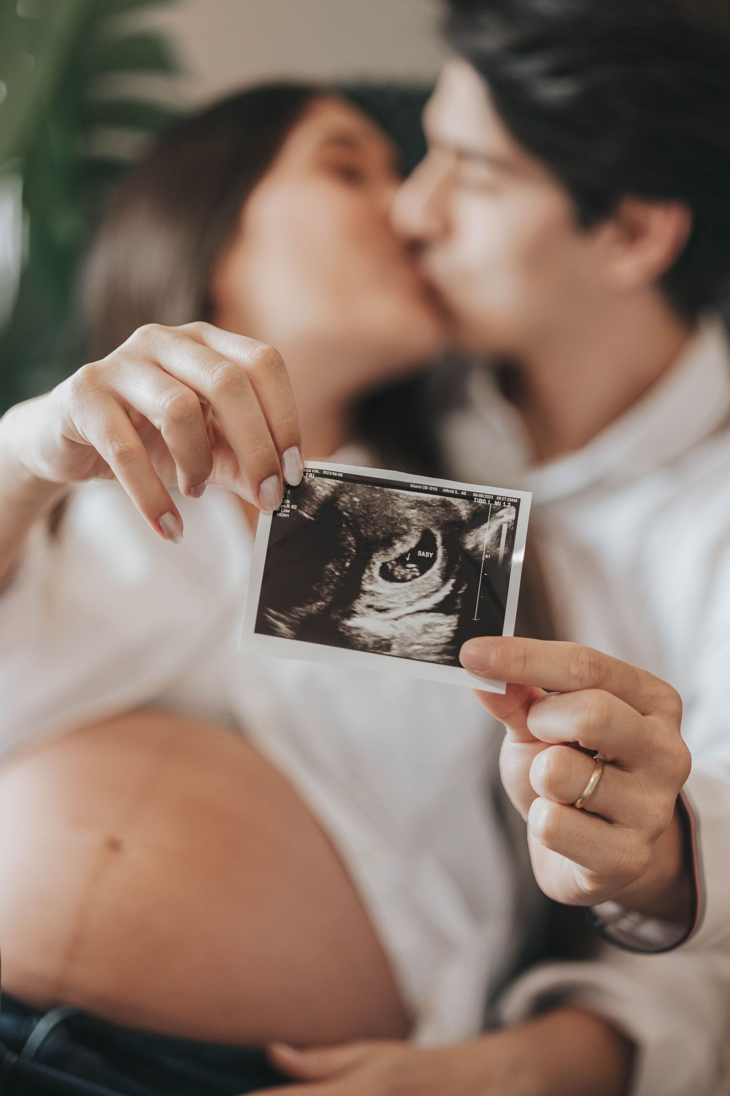 A couple holds up an ultrasound photo while sharing an intimate moment.