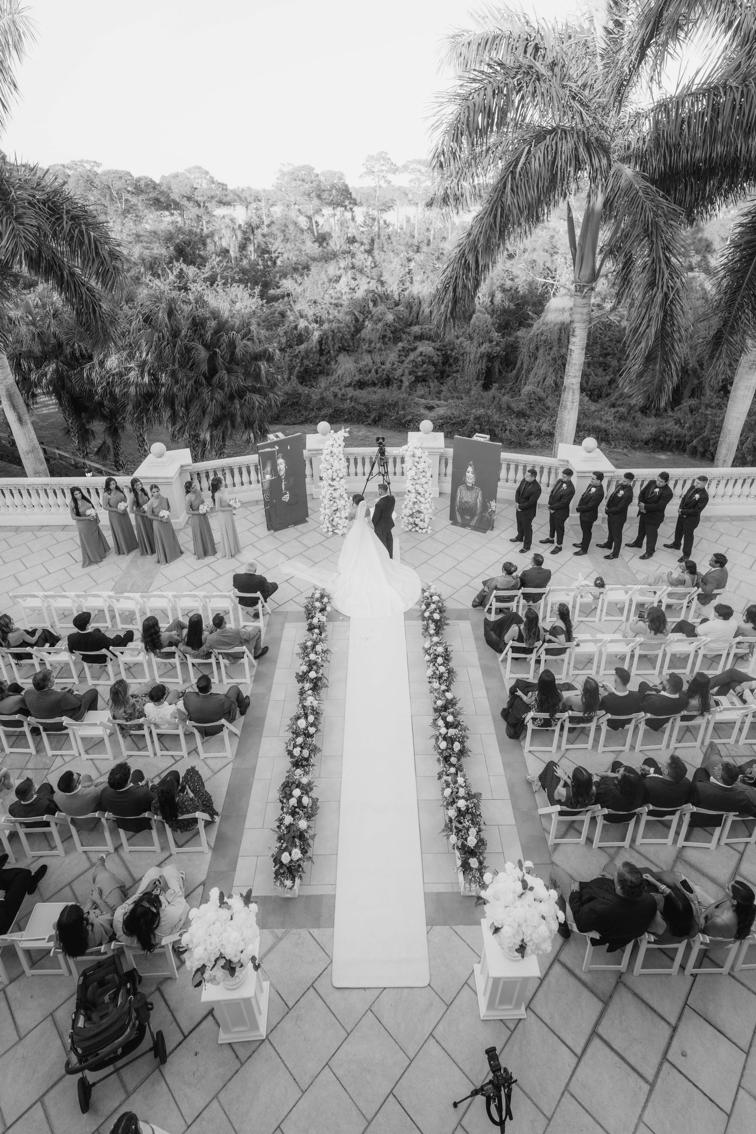 Aerial view of an outdoor wedding ceremony setup with white chairs and floral aisle decorations.