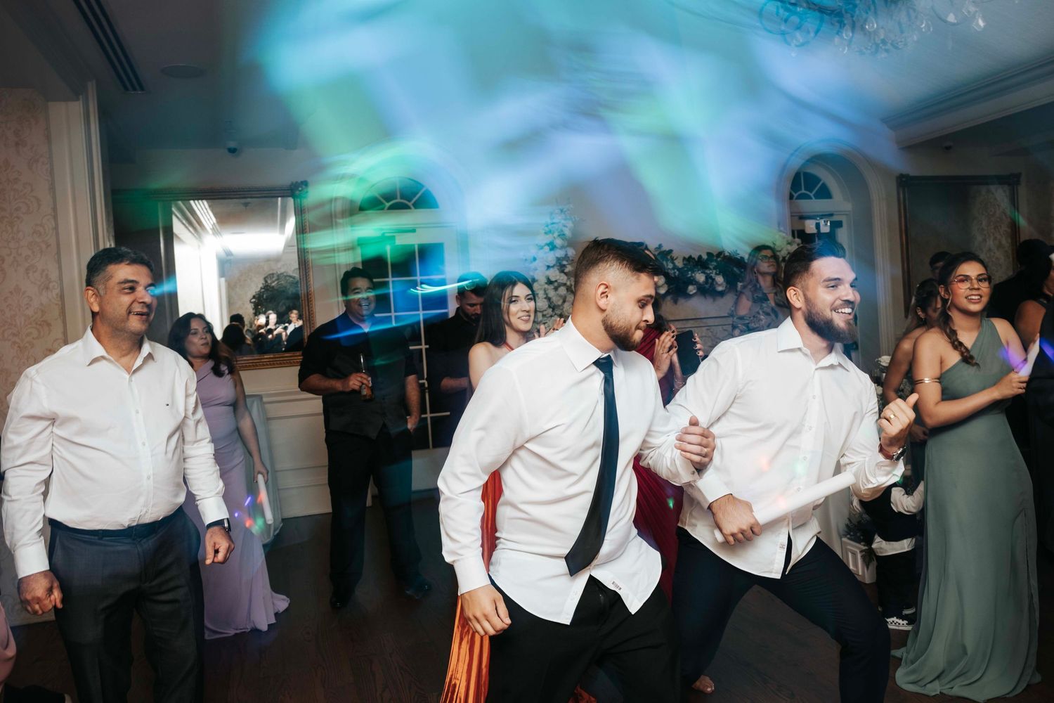 Wedding guests dancing at a reception with colorful blue lighting effects in the background.
