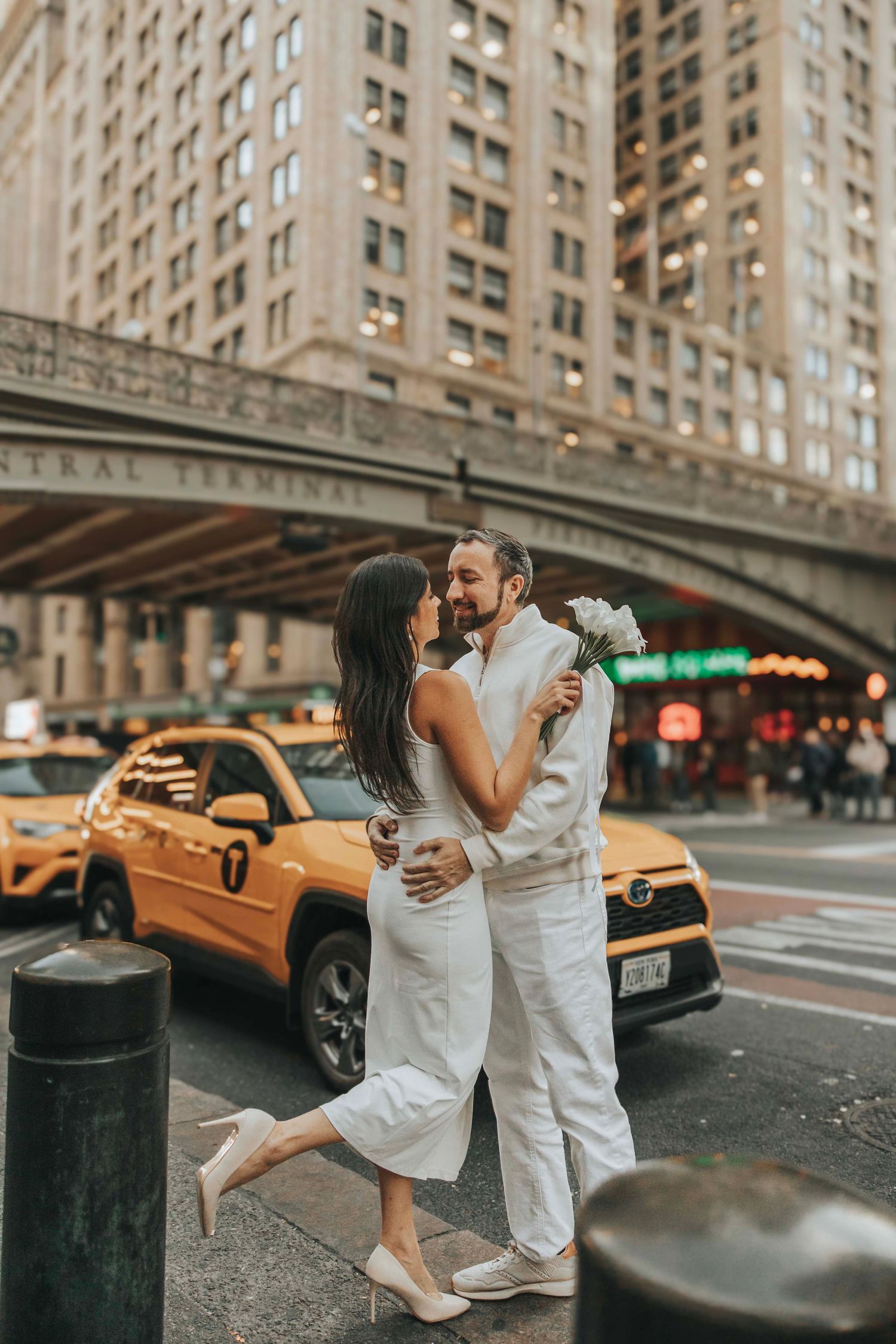 Couple in white embracing under Grand Central Terminal with iconic NYC yellow cab.