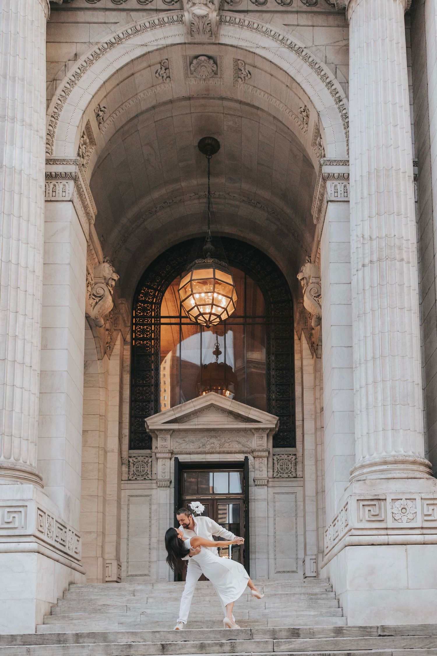 Dancing couple in white attire under an ornate classical archway.