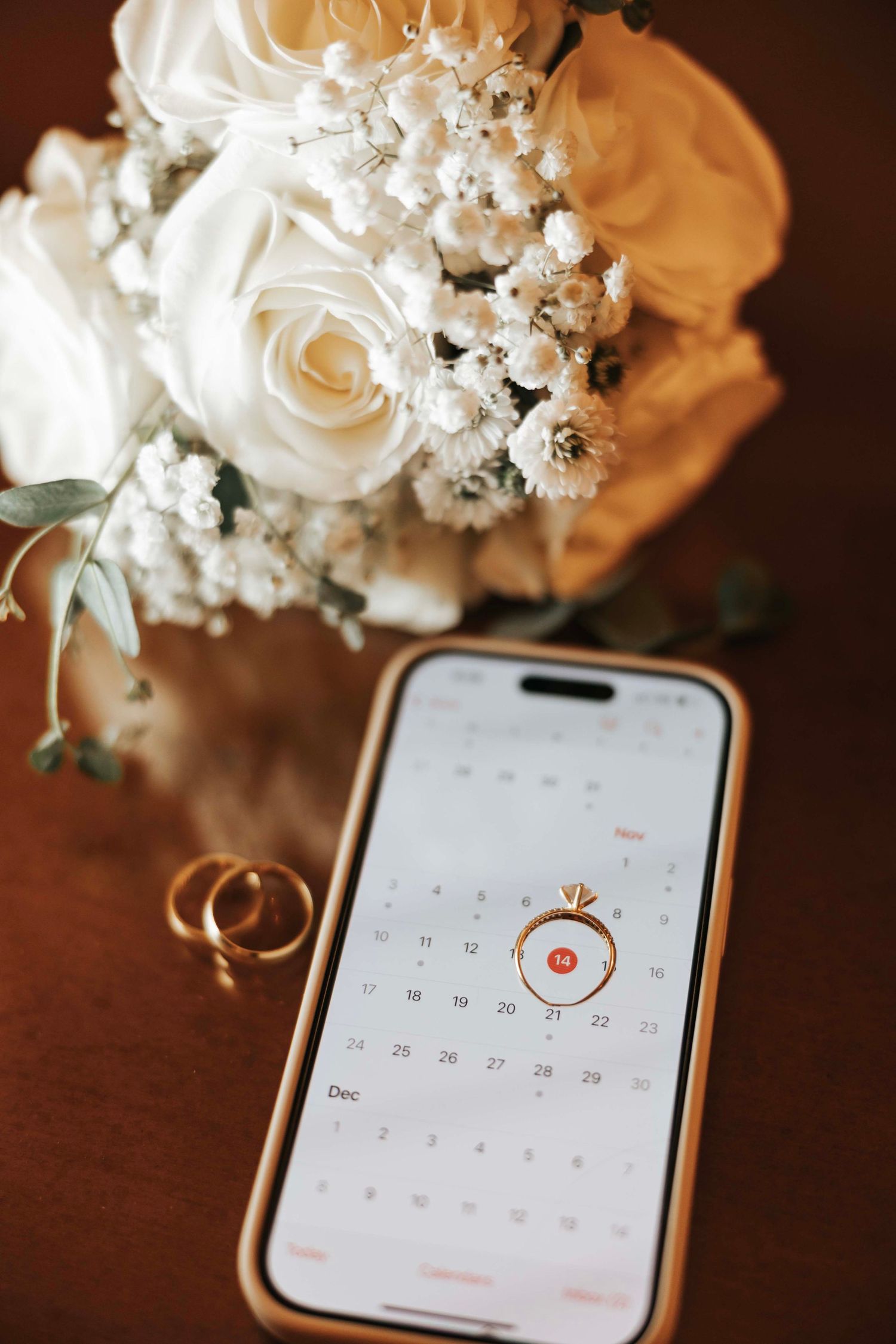 Wedding details with white roses, baby's breath bouquet, wedding rings and phone calendar displayed.