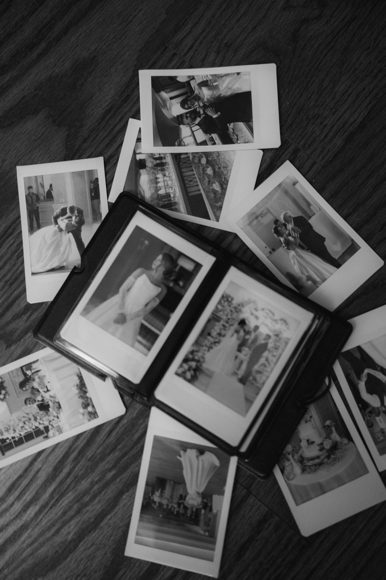 Collection of black and white polaroid photos scattered on dark wooden surface.
