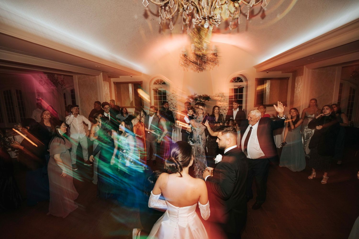 Wedding reception dance floor with motion blur of guests dancing under crystal chandeliers.