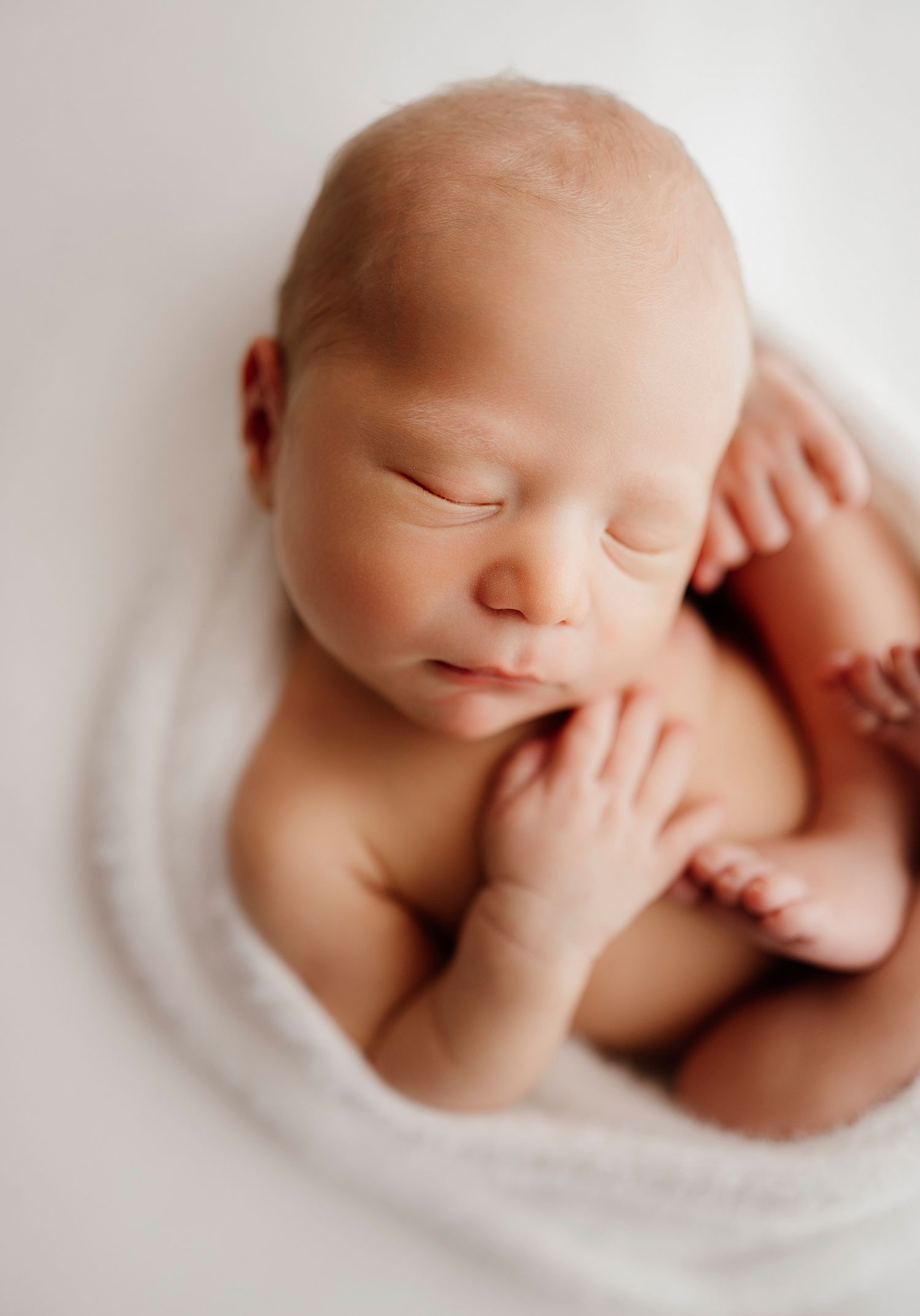 Noworodek w sesji white, Sesja noworodkowa Jasło – śpiące maleństwo w koszu, owinięte w miękką tkaninę w kolorze beżowym