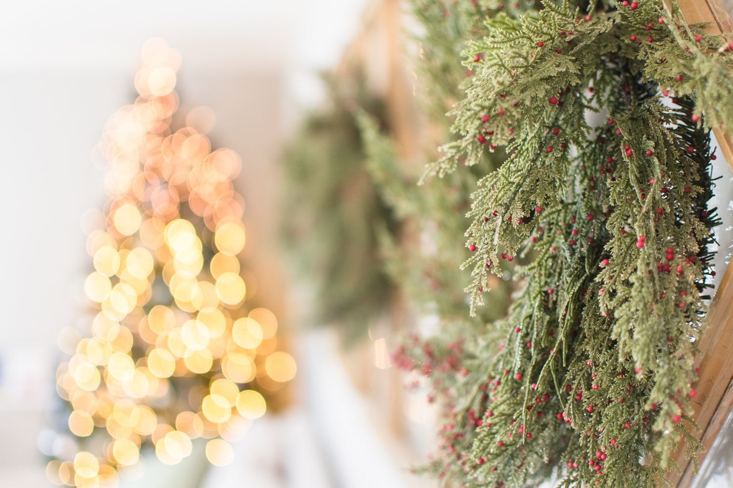 Evergreen garland with twinkling lights and ornaments hangs elegantly against a white wall creating a festive holiday display.