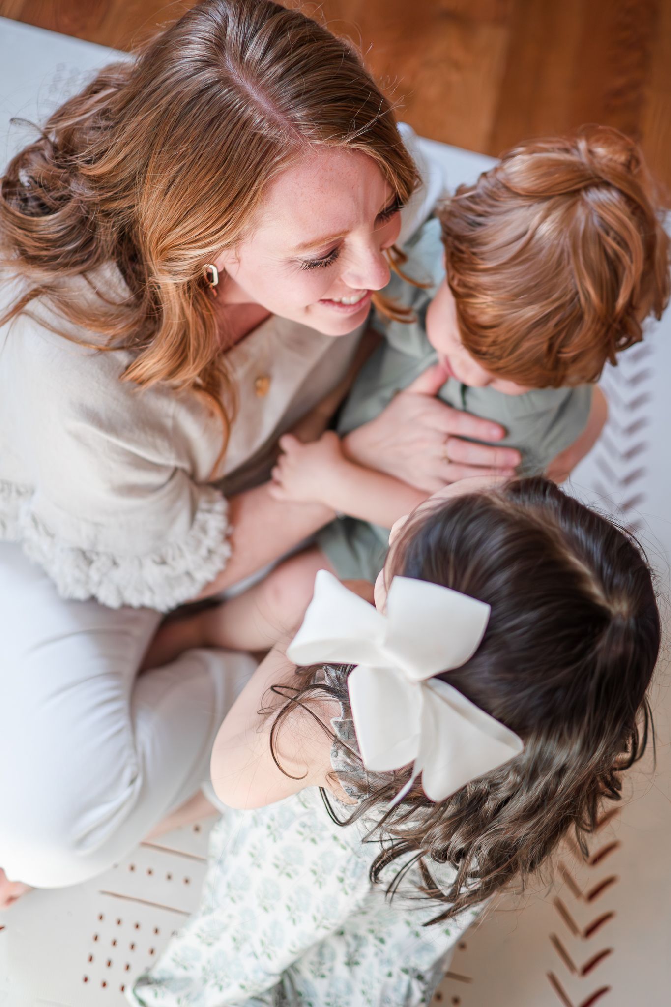 Top-down view of people in white lace dresses sharing an intimate family moment together on a patterned blanket.