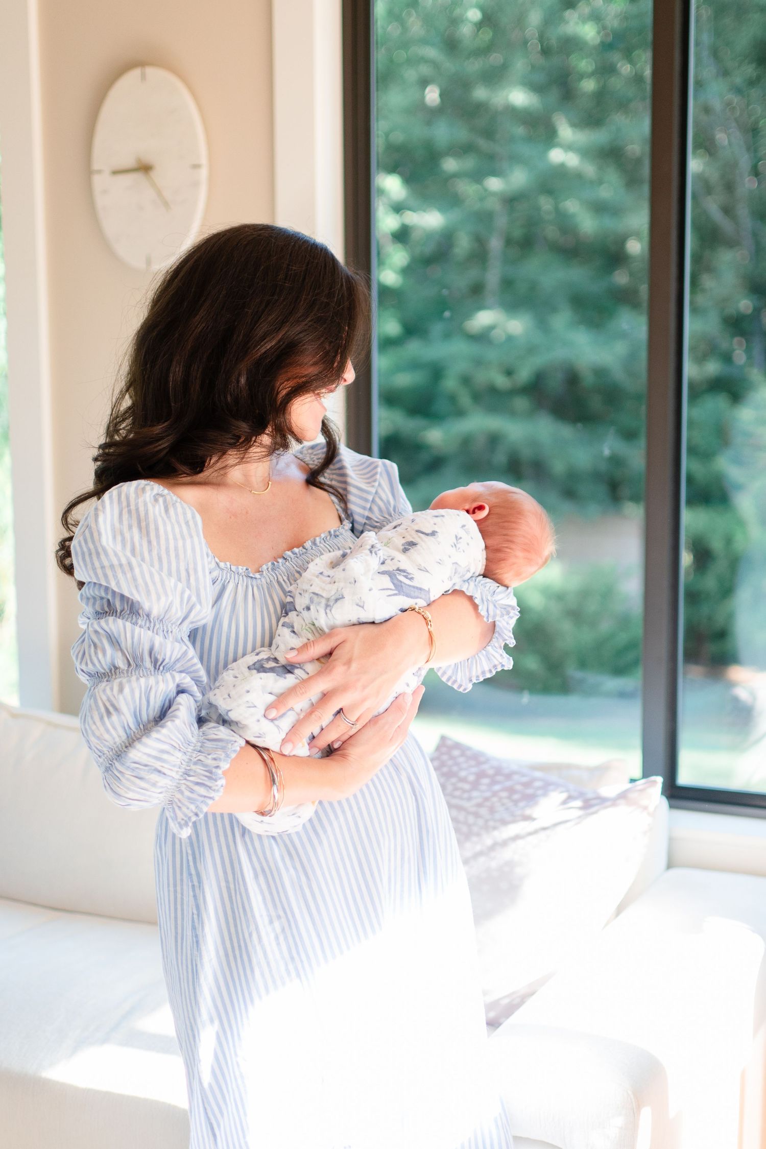 A tender moment captured in natural light as an infant in white lace is held gently against a blue striped dress.