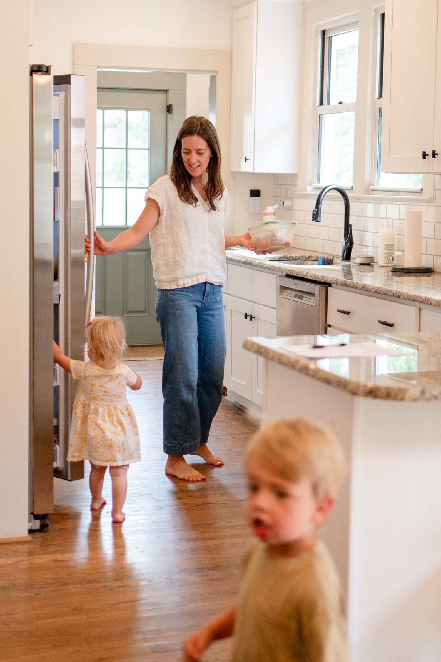 A family gathers in a bright modern kitchen with white cabinets, granite countertops and hardwood floors.