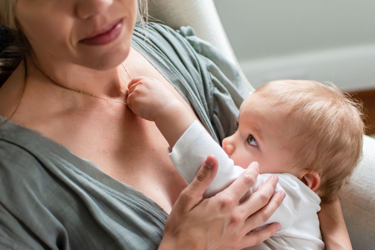 A tender moment of breastfeeding as a baby in white clothing nurses while being cradled.