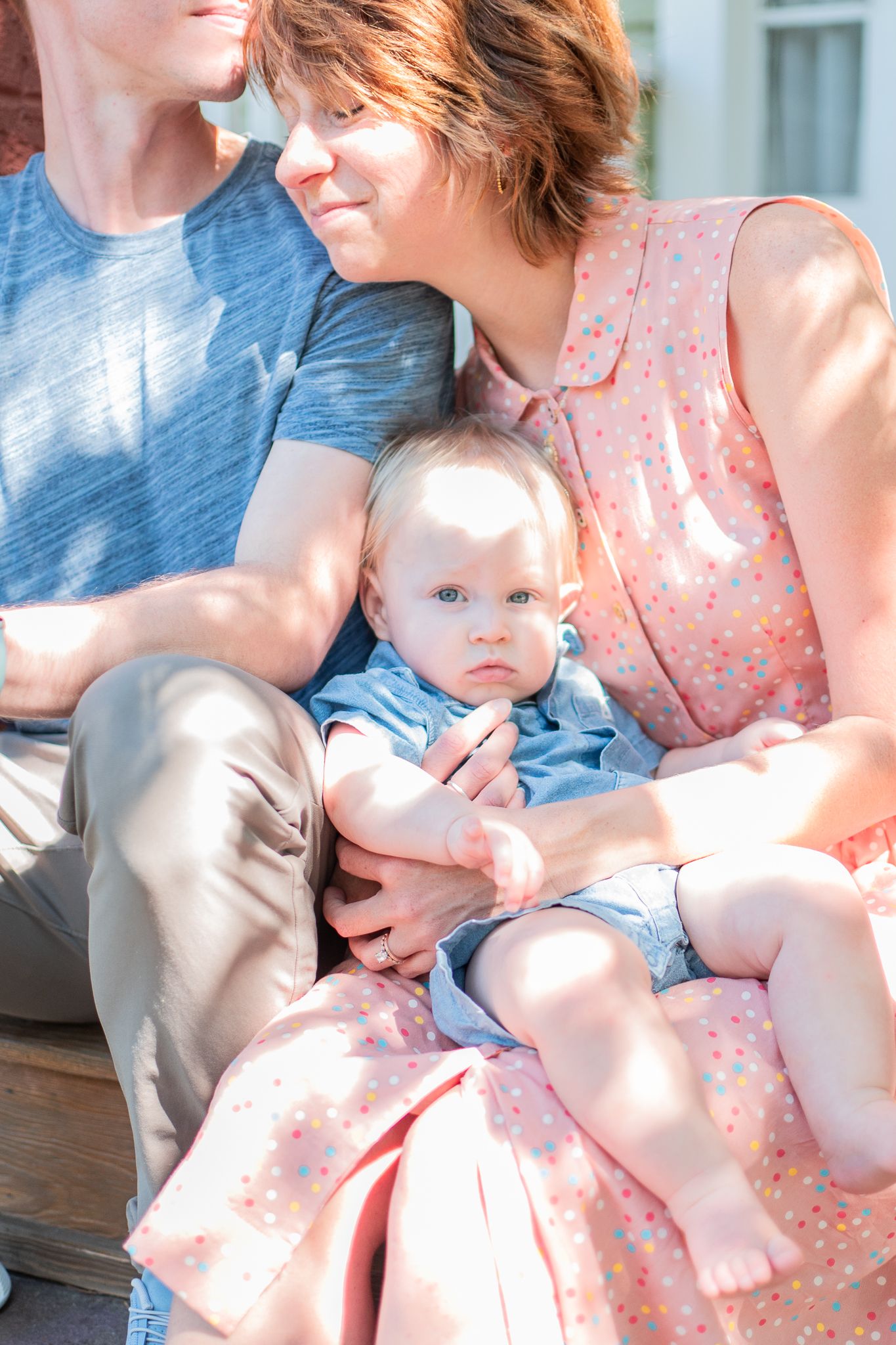 Family sits on front porch with the light filtering through the trees during their family photo shoot.