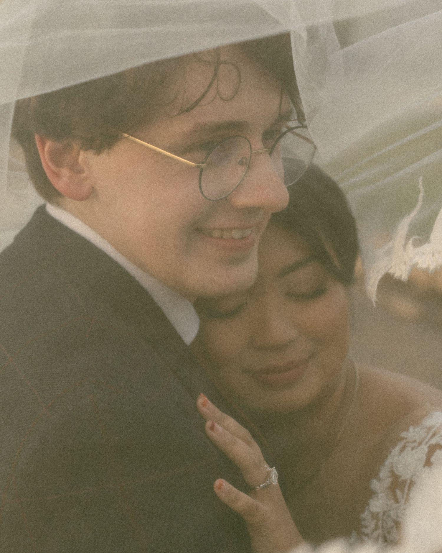 A romantic wedding photo showing a close embrace between a couple under soft tulle and a dreamy vintage filter effect.
