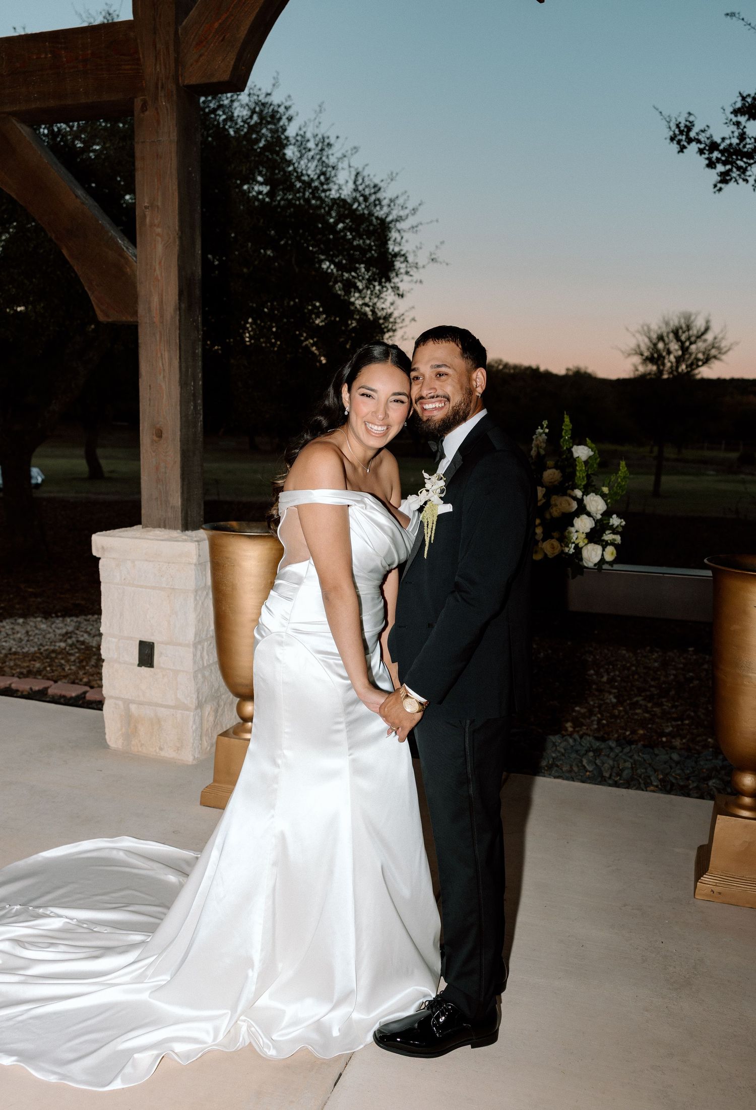 A bride and groom share a joyful moment together at their outdoor wedding venue during sunset.