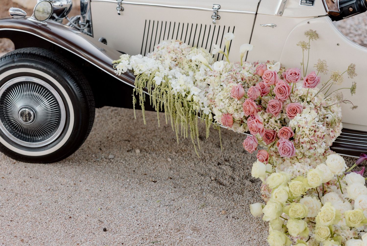 Vintage car decorated with cascading white and pink floral arrangements on the ground.