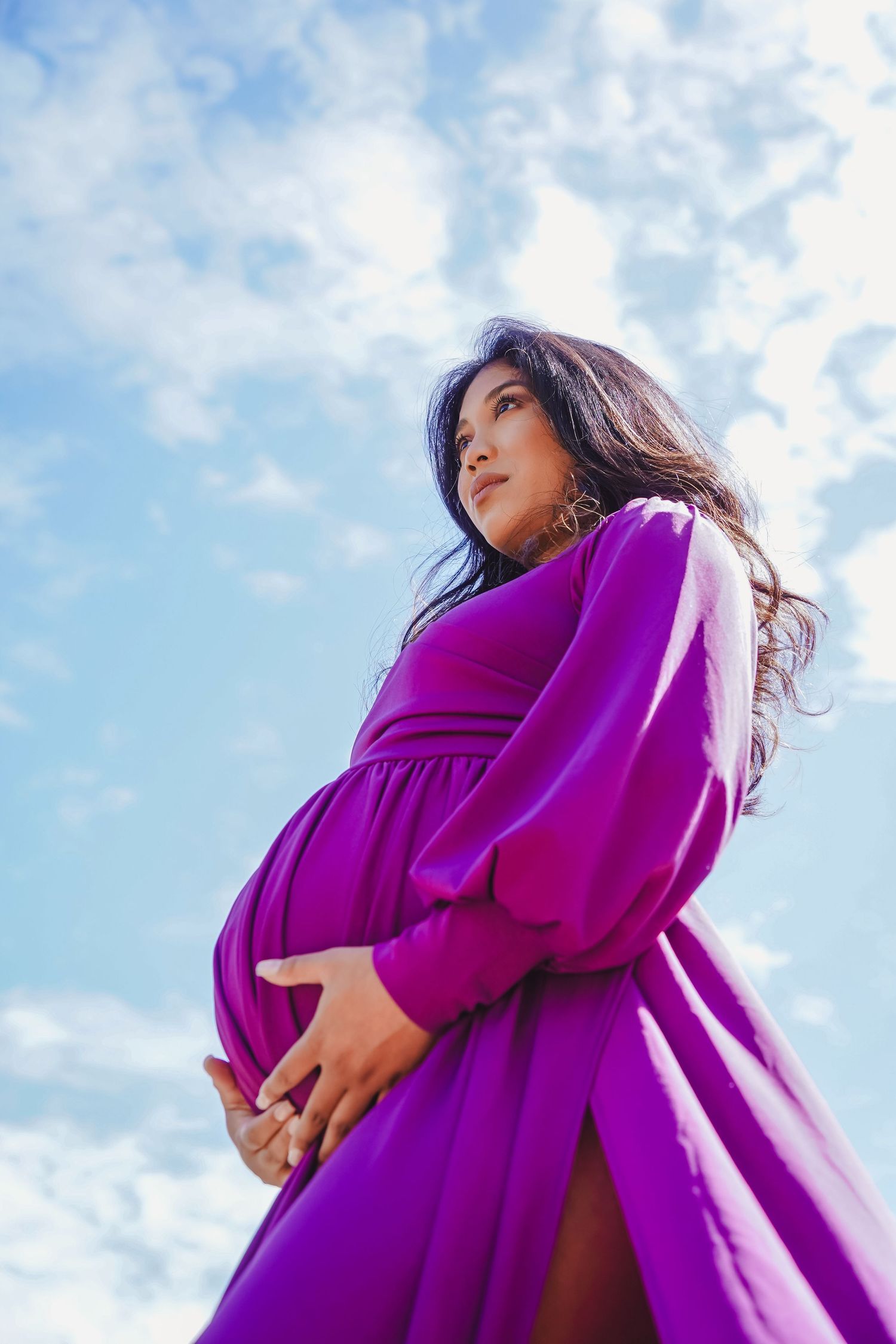 Low angle view of woman in flowing purple dress against blue sky with clouds.