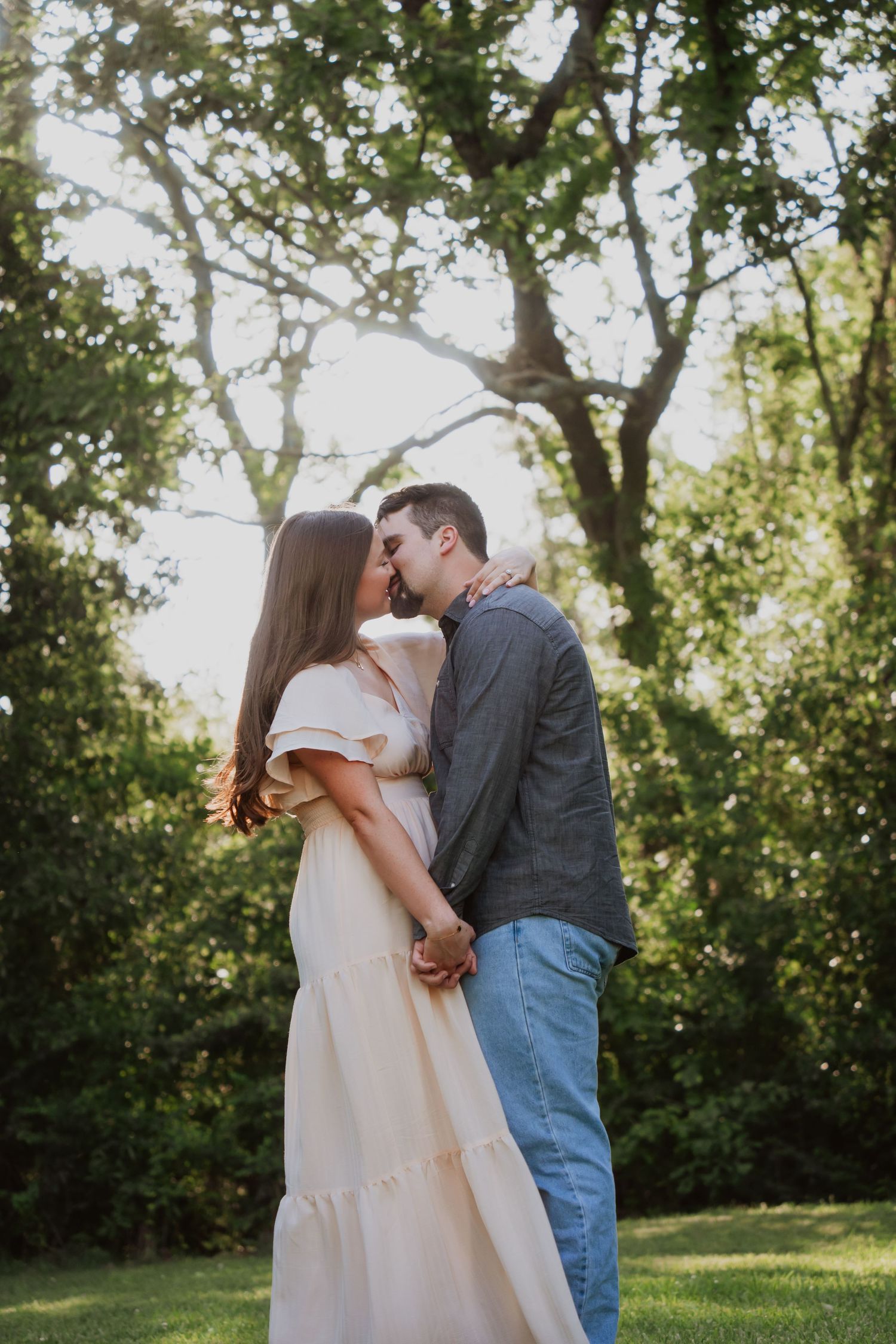 Romantic couple in white dress and gray jacket sharing tender moment outdoors.