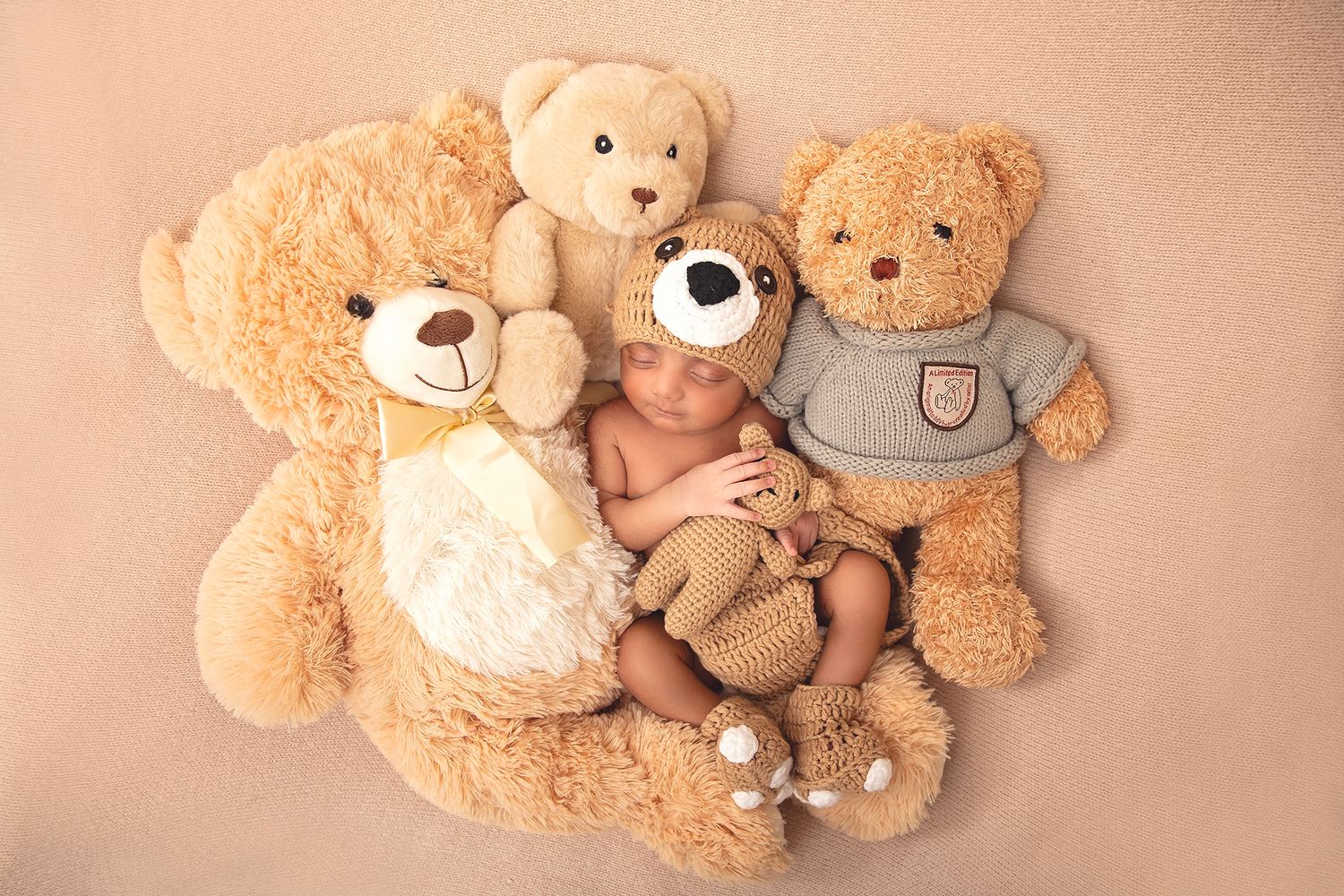 Newborn baby sleeping peacefully surrounded by three soft tan teddy bears on a beige background.