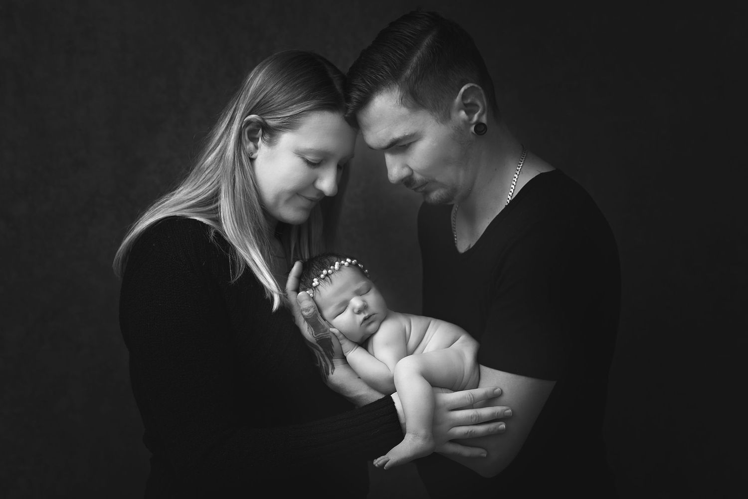 Black and white photo of parents tenderly holding their sleeping newborn baby, studio portrait.