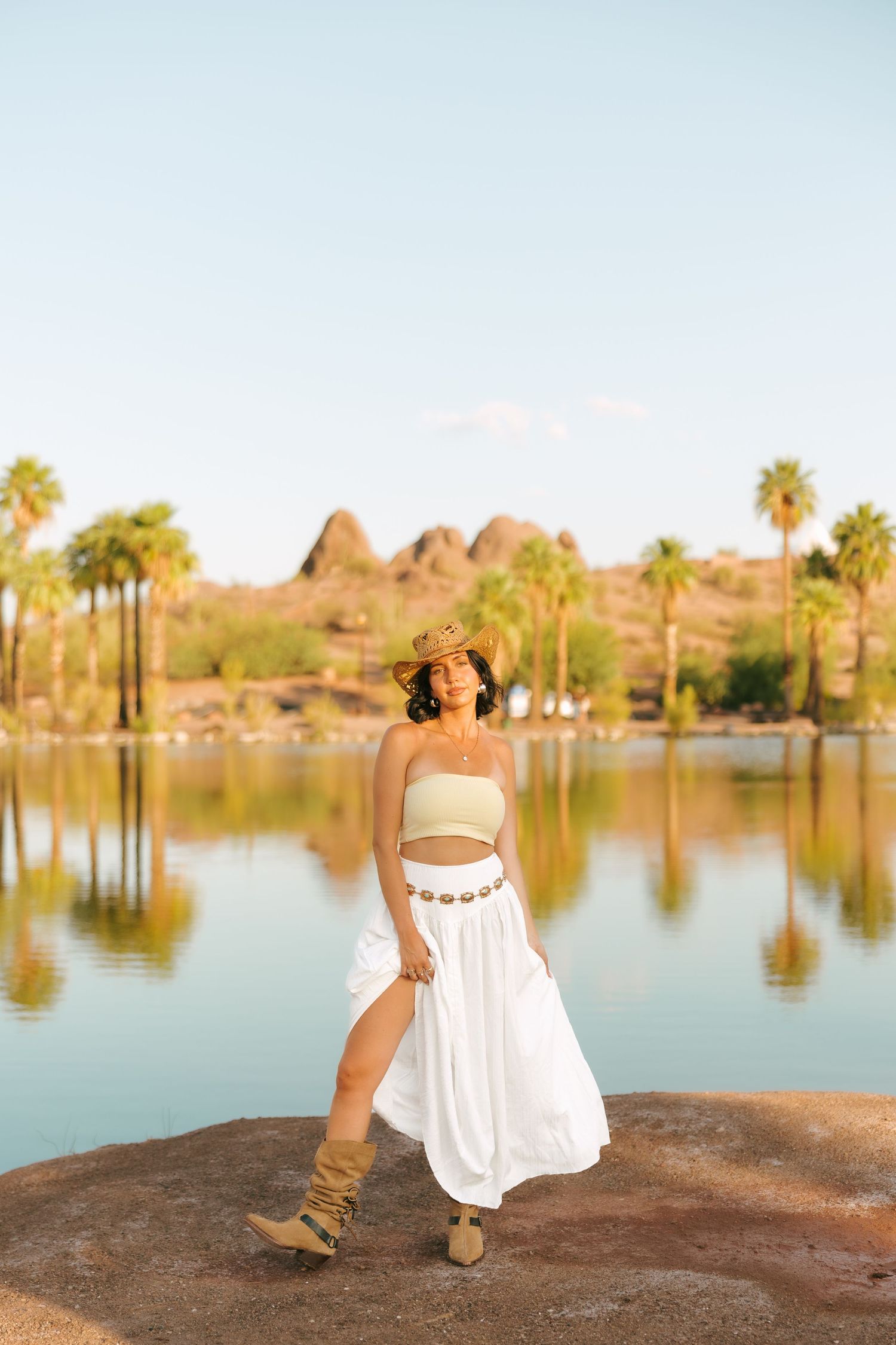 Scenic lakeside view with palm trees and mountain backdrop in golden sunlight.