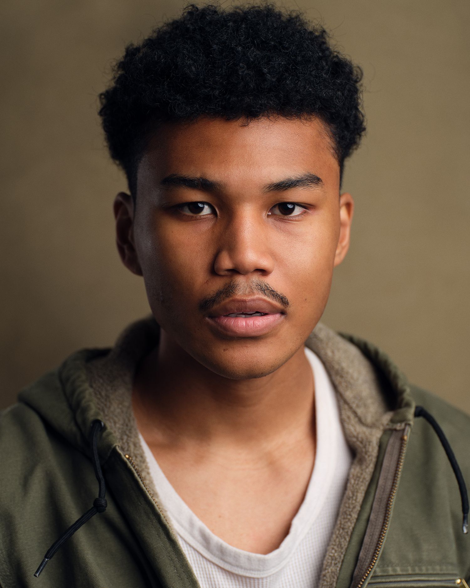 Dark, moody headshot of a NYC student actor in greens.