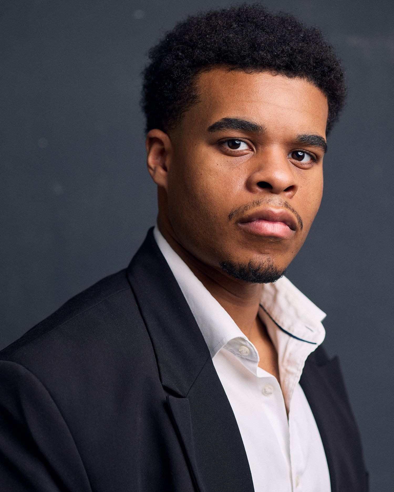 Professional headshot of a NYC actor on a dark, moody background. He has a serious expression.