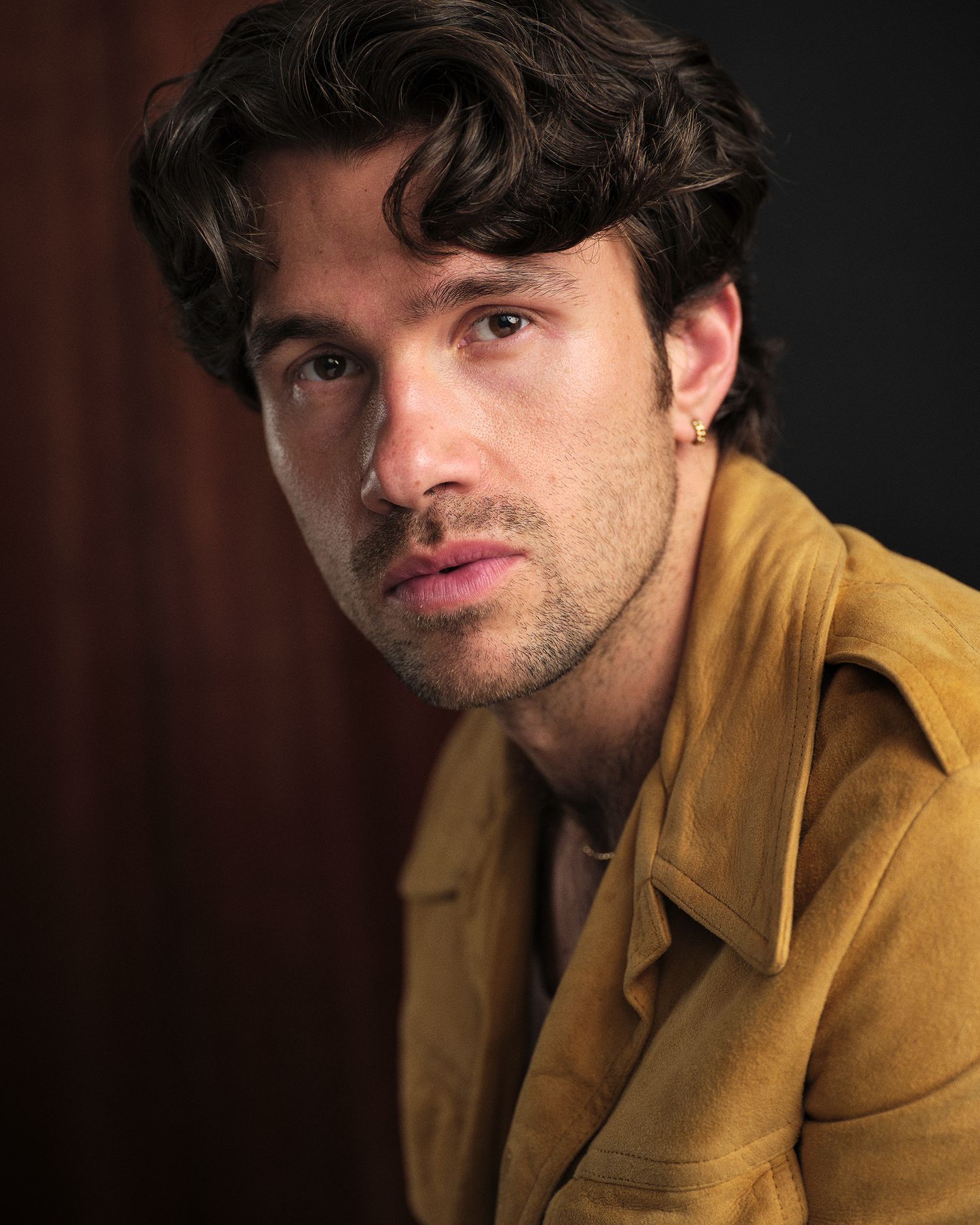 Moody headshot of a male actor in his 30s wearing a yellow jacket.