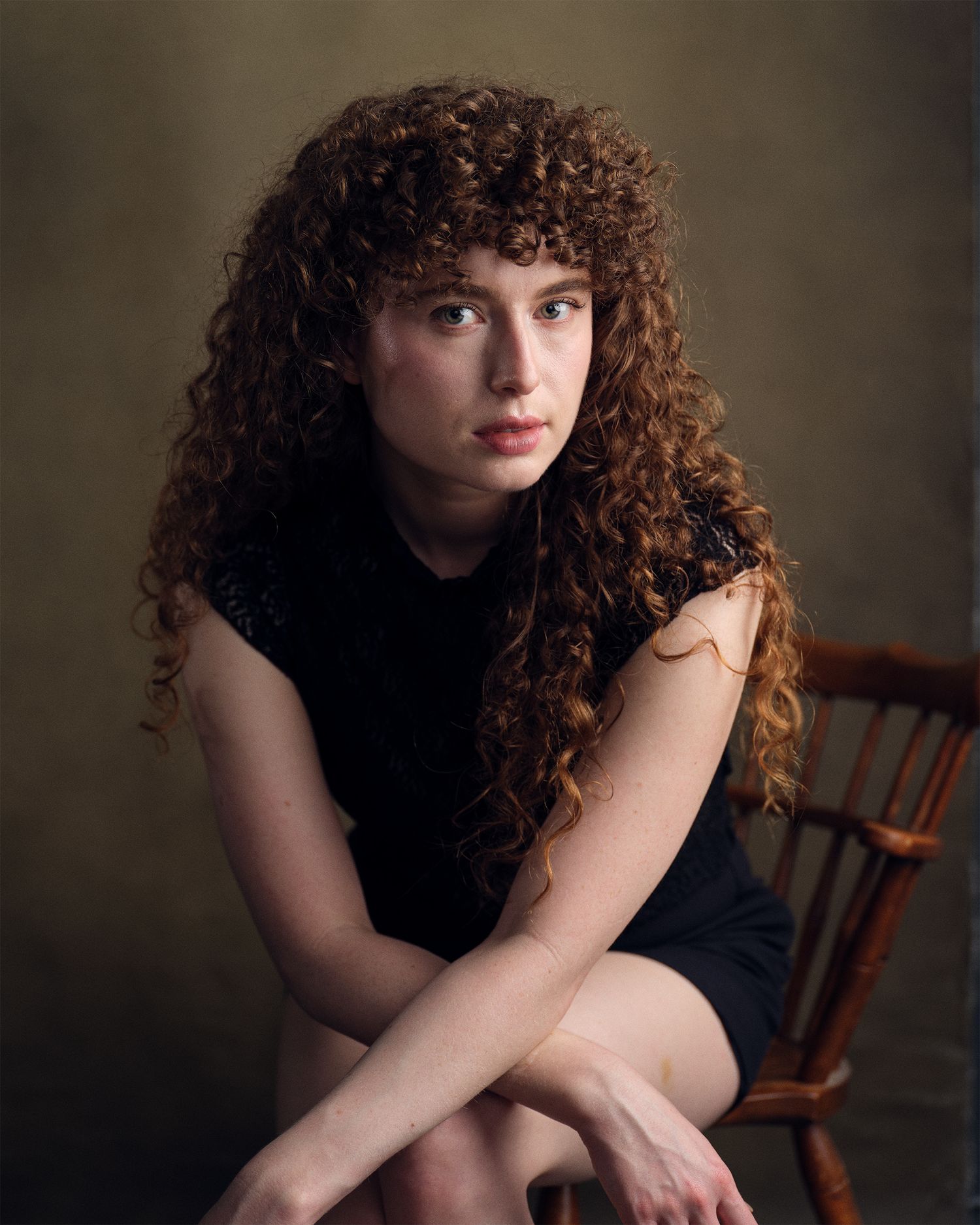 Dramatic and moody portrait of an artist leaning forward while posing in a chair.