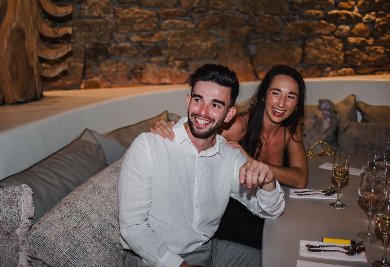 Couple enjoying dinner at an intimate restaurant table against a stone wall background.