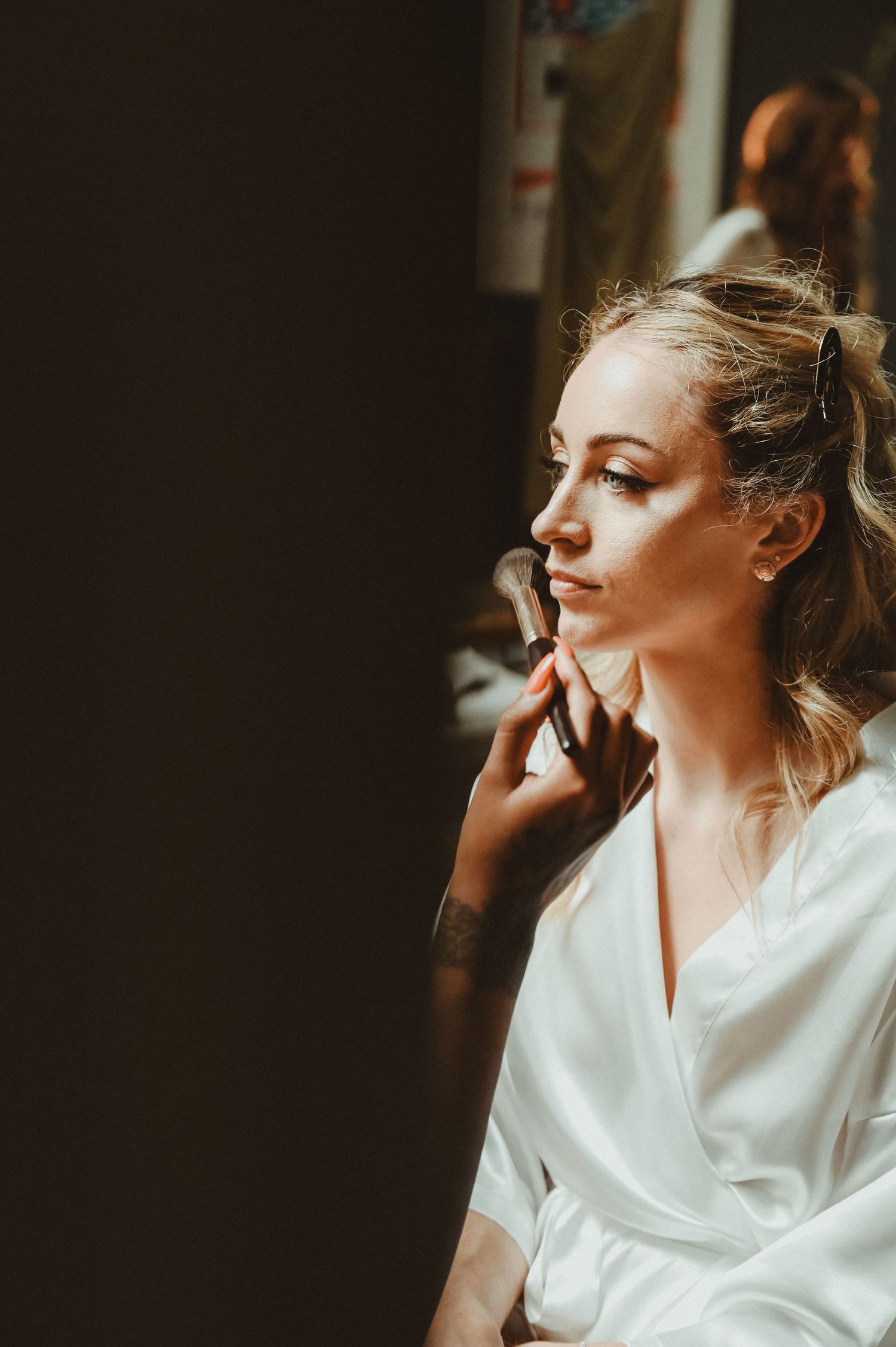 Side profile of someone in a white robe during makeup application in natural light.