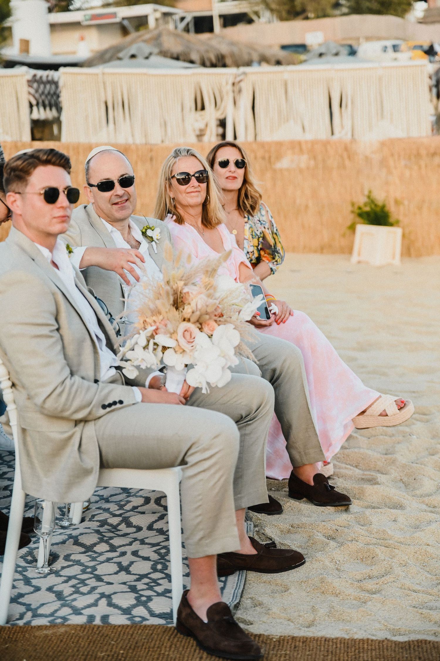 Wedding guests in formal attire seated at a beachside ceremony with decorative details.