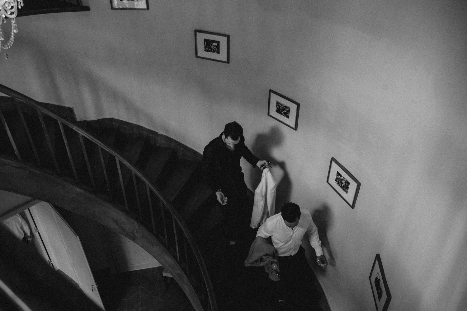 A black and white image of people descending a curved staircase lined with framed artwork.