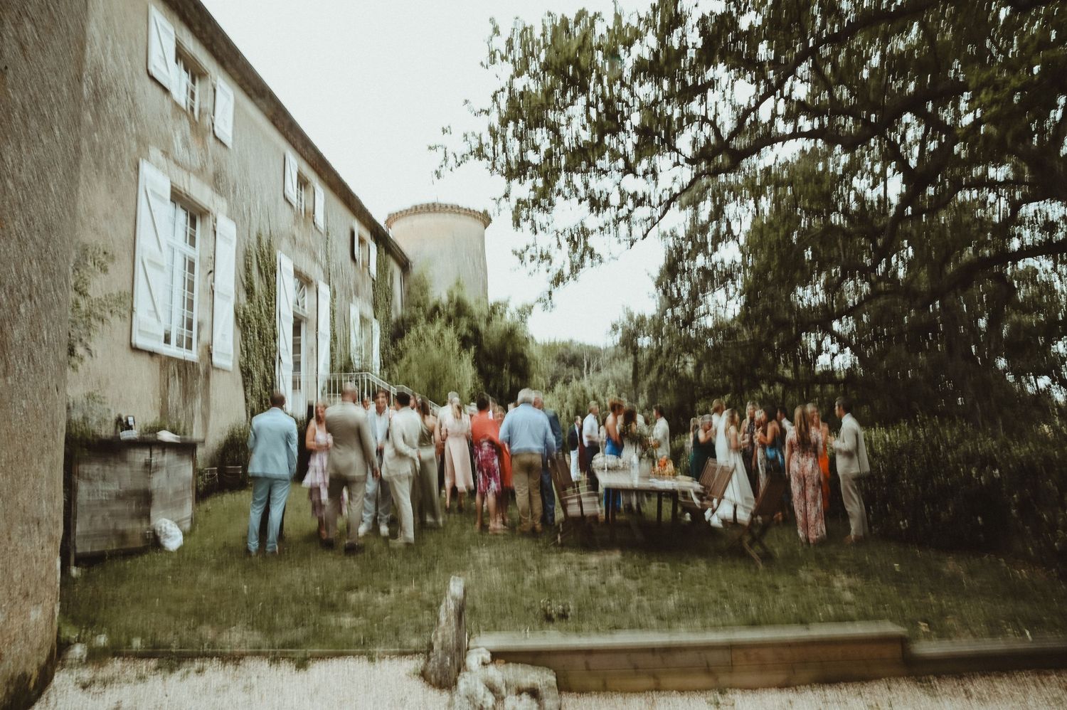 Large group of wedding guests gathered outside historic stone building for reception.