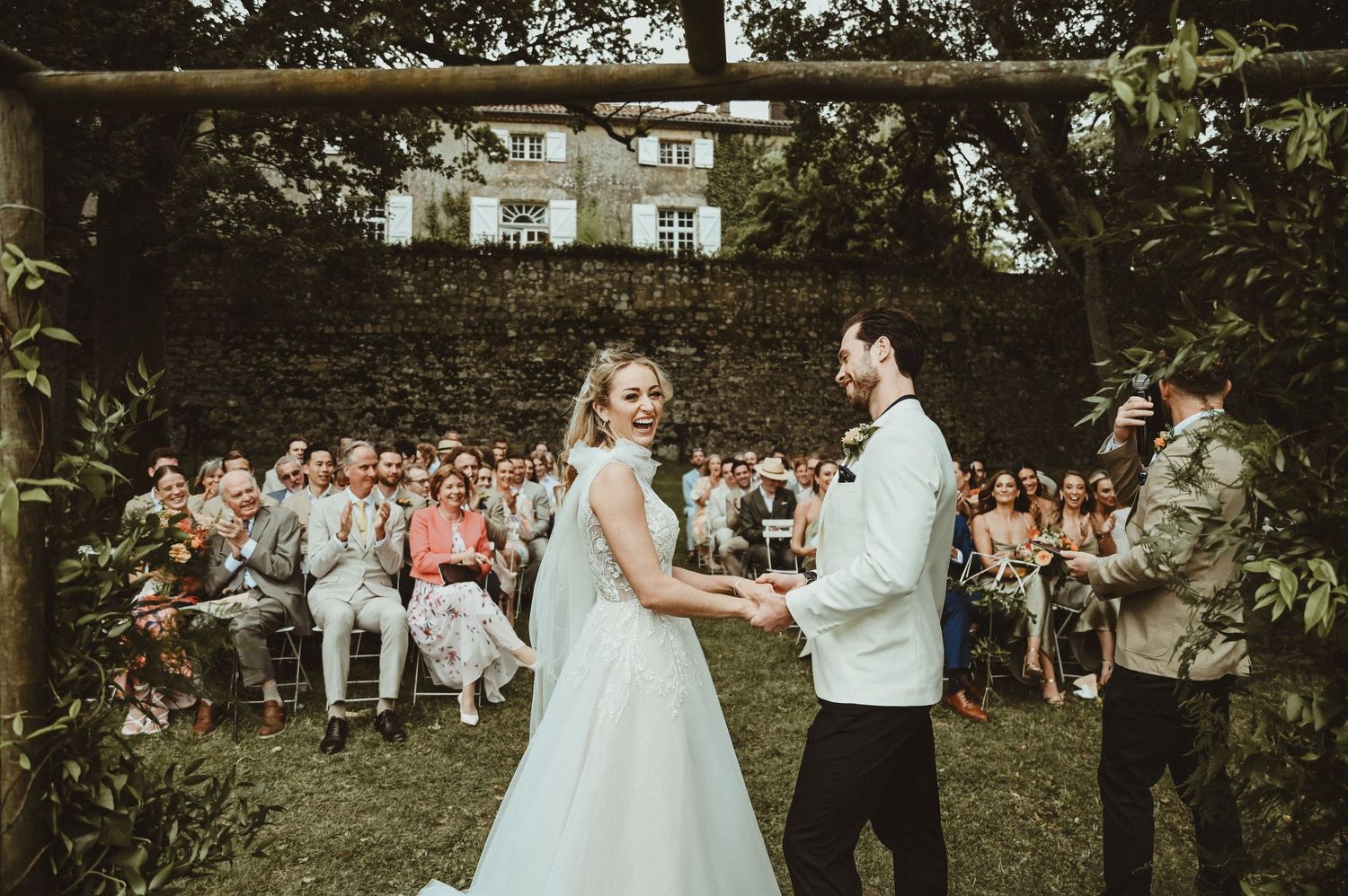 A couple celebrates during their wedding ceremony with guests seated in the background.