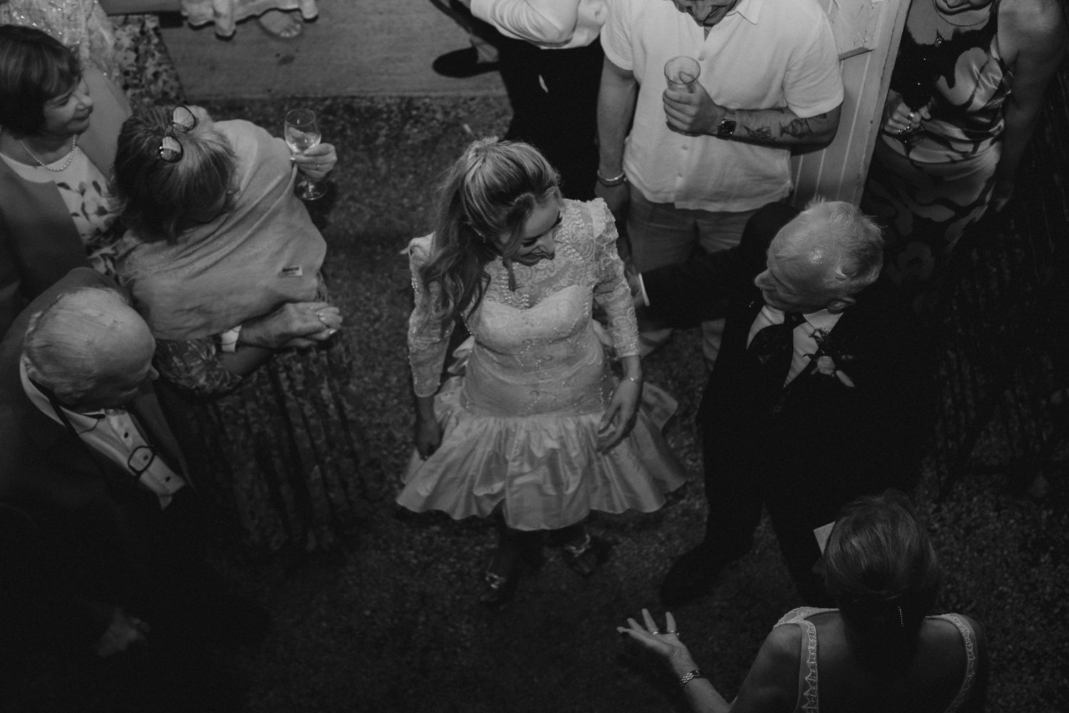 A black and white photograph of wedding guests dancing at a reception.