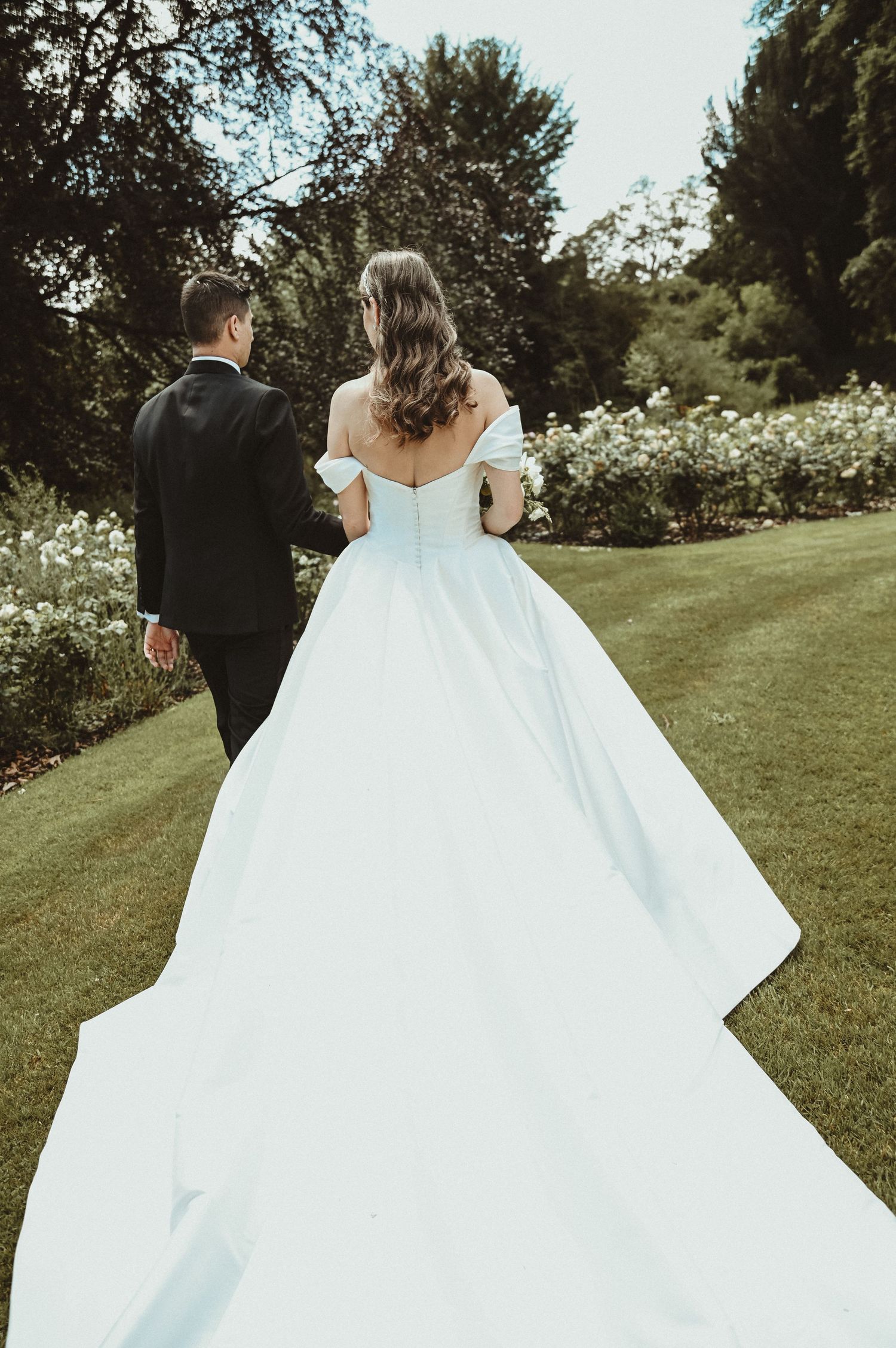 A sweeping view of a wedding dress train as couple walks through garden path.