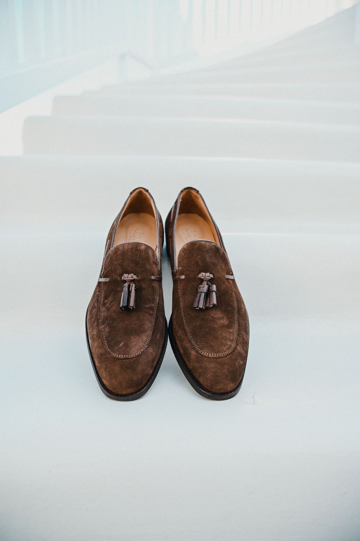 Brown suede tassel loafers displayed against a white background.